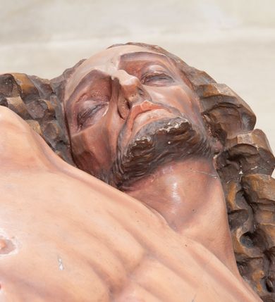 Zdjęcie nr 13: Rzeźba ustawiona na niewysokim, prostopadłościennym postumencie oraz na konsoli w kształcie fragmentu pilastra o kanelowanym trzonie i kapitelu dekorowanego motywem wolich oczu. Na tle krzyża z luźno przewieszoną przez poziomą belkę białą tkaniną ukazani Maria oraz martwy Chrystus. Jezus o szczupłym, muskularnym ciele z widocznymi śladami męki ukazany w pozycji półleżącej z torsem i ramionami wspartymi o postać Marii. Ręce ułożone luźno wzdłuż ciała. Głowa Chrystusa opada na prawe ramię postaci; twarz szczupła z wyraźnie zarysowanymi kośćmi policzkowymi, oczy zamknięte. Długie, brązowe włosy z przedziałkiem pośrodku głowy skręcają się w spiralne loki. Na twarzy krótki zarost. Wokół bioder Chrystusa luźno owinięte białe perizonium. Maria ukazana w pozycji klęczącej z rękoma uniesionymi na boki w dynamicznym geście. Głowa pochylona nieznacznie do dołu, w kierunku ciała Chrystusa. Twarz Marii szczupła, owalna z głęboko osadzonymi, dużymi oczami oraz wydatnym, prostym nosem. Postać ubrana jest w czerwoną suknię z długimi rękawami, niebieski płaszcz oraz białą chustę z podwiką wokół szyi. Po lewej stronie kompozycji, spod sukni widoczna jest bosa stopa.  