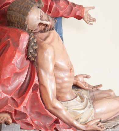 Zdjęcie nr 10: Rzeźba ustawiona na niewysokim, prostopadłościennym postumencie oraz na konsoli w kształcie fragmentu pilastra o kanelowanym trzonie i kapitelu dekorowanego motywem wolich oczu. Na tle krzyża z luźno przewieszoną przez poziomą belkę białą tkaniną ukazani Maria oraz martwy Chrystus. Jezus o szczupłym, muskularnym ciele z widocznymi śladami męki ukazany w pozycji półleżącej z torsem i ramionami wspartymi o postać Marii. Ręce ułożone luźno wzdłuż ciała. Głowa Chrystusa opada na prawe ramię postaci; twarz szczupła z wyraźnie zarysowanymi kośćmi policzkowymi, oczy zamknięte. Długie, brązowe włosy z przedziałkiem pośrodku głowy skręcają się w spiralne loki. Na twarzy krótki zarost. Wokół bioder Chrystusa luźno owinięte białe perizonium. Maria ukazana w pozycji klęczącej z rękoma uniesionymi na boki w dynamicznym geście. Głowa pochylona nieznacznie do dołu, w kierunku ciała Chrystusa. Twarz Marii szczupła, owalna z głęboko osadzonymi, dużymi oczami oraz wydatnym, prostym nosem. Postać ubrana jest w czerwoną suknię z długimi rękawami, niebieski płaszcz oraz białą chustę z podwiką wokół szyi. Po lewej stronie kompozycji, spod sukni widoczna jest bosa stopa.  