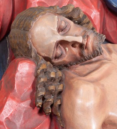Zdjęcie nr 11: Rzeźba ustawiona na niewysokim, prostopadłościennym postumencie oraz na konsoli w kształcie fragmentu pilastra o kanelowanym trzonie i kapitelu dekorowanego motywem wolich oczu. Na tle krzyża z luźno przewieszoną przez poziomą belkę białą tkaniną ukazani Maria oraz martwy Chrystus. Jezus o szczupłym, muskularnym ciele z widocznymi śladami męki ukazany w pozycji półleżącej z torsem i ramionami wspartymi o postać Marii. Ręce ułożone luźno wzdłuż ciała. Głowa Chrystusa opada na prawe ramię postaci; twarz szczupła z wyraźnie zarysowanymi kośćmi policzkowymi, oczy zamknięte. Długie, brązowe włosy z przedziałkiem pośrodku głowy skręcają się w spiralne loki. Na twarzy krótki zarost. Wokół bioder Chrystusa luźno owinięte białe perizonium. Maria ukazana w pozycji klęczącej z rękoma uniesionymi na boki w dynamicznym geście. Głowa pochylona nieznacznie do dołu, w kierunku ciała Chrystusa. Twarz Marii szczupła, owalna z głęboko osadzonymi, dużymi oczami oraz wydatnym, prostym nosem. Postać ubrana jest w czerwoną suknię z długimi rękawami, niebieski płaszcz oraz białą chustę z podwiką wokół szyi. Po lewej stronie kompozycji, spod sukni widoczna jest bosa stopa.  