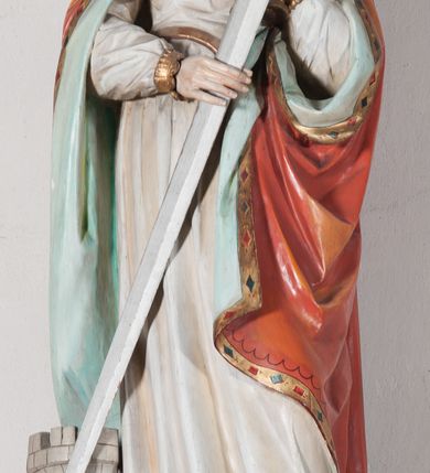 Zdjęcie nr 9: Rzeźba drążona, ustawiona na niewielkim, prostopadłościennym postumencie o ściętych narożach oraz rozbudowanej, neobarokowej konsoli. Święta ukazana frontalnie, w pozycji stojącej z kielichem w lewej dłoni i mieczem w prawej. Barbara została przedstawiona jako młoda, jasnowłosa kobieta o owalnej twarzy, dużych, niebieskich oczach i wydatnym nosie. Ubrana jest w strój królewski złożony z długiej, białej sukni ze złotymi elementami oraz czerwonego płaszcza z seledynowym podbiciem. Płaszcz jest spięty pod szyją ozdobną, złotą broszą. Na głowie postaci złota, wysadzana kamieniami szlachetnymi korona w typie otwartym. U jej stóp z lewej strony przedstawiona owalna wieża zwieńczona krenelażem. Konsola, na której ustawiona jest rzeźba wspierana jest przez postać jasnowłosego anioła w niebieskiej szacie trzymającego w rękach banderolę z napisem „Św(ięta) BARBARO Módl się za nami”. Anioł umieszczony na tle srebrzonego obłoku; banderola, skrzydła anioła oraz detale architektoniczne konsoli złocone.