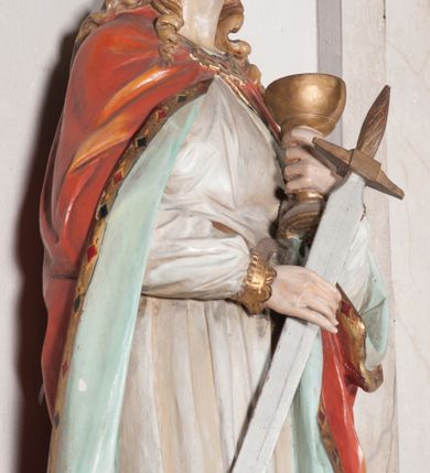 Zdjęcie nr 13: Rzeźba drążona, ustawiona na niewielkim, prostopadłościennym postumencie o ściętych narożach oraz rozbudowanej, neobarokowej konsoli. Święta ukazana frontalnie, w pozycji stojącej z kielichem w lewej dłoni i mieczem w prawej. Barbara została przedstawiona jako młoda, jasnowłosa kobieta o owalnej twarzy, dużych, niebieskich oczach i wydatnym nosie. Ubrana jest w strój królewski złożony z długiej, białej sukni ze złotymi elementami oraz czerwonego płaszcza z seledynowym podbiciem. Płaszcz jest spięty pod szyją ozdobną, złotą broszą. Na głowie postaci złota, wysadzana kamieniami szlachetnymi korona w typie otwartym. U jej stóp z lewej strony przedstawiona owalna wieża zwieńczona krenelażem. Konsola, na której ustawiona jest rzeźba wspierana jest przez postać jasnowłosego anioła w niebieskiej szacie trzymającego w rękach banderolę z napisem „Św(ięta) BARBARO Módl się za nami”. Anioł umieszczony na tle srebrzonego obłoku; banderola, skrzydła anioła oraz detale architektoniczne konsoli złocone.