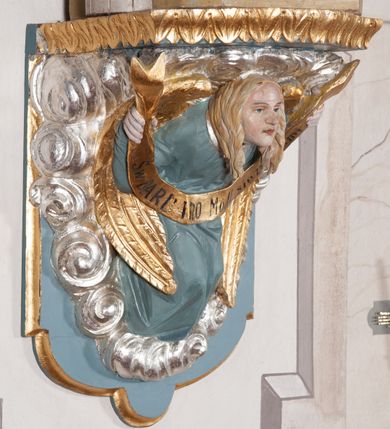 Zdjęcie nr 5: Rzeźba drążona, ustawiona na niewielkim, prostopadłościennym postumencie o ściętych narożach oraz rozbudowanej, neobarokowej konsoli. Święta ukazana frontalnie, w pozycji stojącej z kielichem w lewej dłoni i mieczem w prawej. Barbara została przedstawiona jako młoda, jasnowłosa kobieta o owalnej twarzy, dużych, niebieskich oczach i wydatnym nosie. Ubrana jest w strój królewski złożony z długiej, białej sukni ze złotymi elementami oraz czerwonego płaszcza z seledynowym podbiciem. Płaszcz jest spięty pod szyją ozdobną, złotą broszą. Na głowie postaci złota, wysadzana kamieniami szlachetnymi korona w typie otwartym. U jej stóp z lewej strony przedstawiona owalna wieża zwieńczona krenelażem. Konsola, na której ustawiona jest rzeźba wspierana jest przez postać jasnowłosego anioła w niebieskiej szacie trzymającego w rękach banderolę z napisem „Św(ięta) BARBARO Módl się za nami”. Anioł umieszczony na tle srebrzonego obłoku; banderola, skrzydła anioła oraz detale architektoniczne konsoli złocone.