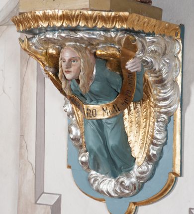 Zdjęcie nr 7: Rzeźba drążona, ustawiona na niewielkim, prostopadłościennym postumencie o ściętych narożach oraz rozbudowanej, neobarokowej konsoli. Święta ukazana frontalnie, w pozycji stojącej z kielichem w lewej dłoni i mieczem w prawej. Barbara została przedstawiona jako młoda, jasnowłosa kobieta o owalnej twarzy, dużych, niebieskich oczach i wydatnym nosie. Ubrana jest w strój królewski złożony z długiej, białej sukni ze złotymi elementami oraz czerwonego płaszcza z seledynowym podbiciem. Płaszcz jest spięty pod szyją ozdobną, złotą broszą. Na głowie postaci złota, wysadzana kamieniami szlachetnymi korona w typie otwartym. U jej stóp z lewej strony przedstawiona owalna wieża zwieńczona krenelażem. Konsola, na której ustawiona jest rzeźba wspierana jest przez postać jasnowłosego anioła w niebieskiej szacie trzymającego w rękach banderolę z napisem „Św(ięta) BARBARO Módl się za nami”. Anioł umieszczony na tle srebrzonego obłoku; banderola, skrzydła anioła oraz detale architektoniczne konsoli złocone.