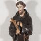 Zdjęcie nr 1: Rzeźba pełnoplastyczna, umieszczona na niewielkim prostopadłościennym postumencie o ściętych narożach oraz złoconej i srebrzonej konsoli utworzonej z liści akantu i róż. Święty ukazany całopostaciowo, frontalnie w pozycji stojącej. Franciszek został przedstawiony jako dojrzały mężczyzna o podłużnej, szczupłej twarzy i krótkich, brązowych włosach i brodzie. Ma duże, ciemne oczy wpatrzone przed siebie, wydatny ostro zakończony nos, usta zamknięte. Postać w prawej ręce trzyma krucyfiks, a lewą dłoń składa na piersi. Święty ubrany jest w długi, ciemnobrązowy habit franciszkański. Do sznura z trzema węzłami ujmującego go w pasie przywiązany jest różaniec. Spod habitu widoczne stopy obute w sandały. Na podstawie, na której ustawiona jest rzeźba widnieje napis „Św(ięty) FRANCISZEK”, na konsoli „ŚWIĘTY FRANCISZKU MÓDL SIĘ ZA NAMI”.