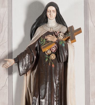 Zdjęcie nr 1: Rzeźba ustawiona na niewielkim, prostopadłościennym postumencie oraz rozbudowanej, neobarokowej konsoli. Święta ukazana frontalnie, w pozycji stojącej z prawą ręką wyciągniętą na bok oraz lewą złożoną na piersi, podtrzymującą krzyż opleciony różami. Teresa została ukazana jako młoda kobieta o owalnej twarzy, dużych oczach i wydatnym nosie. Ubrana jest w ciemnobrązowy, karmelitański habit z jasnym płaszczem. Konsola, na której ustawiona jest rzeźba wspierana jest przez postać jasnowłosego anioła w beżowej szacie trzymającego w rękach banderolę z napisem „Św(ięta) TERESO Módl się za nami&quot;. Anioł umieszczony na tle srebrzonego obłoku; banderola, skrzydła anioła oraz detale architektoniczne konsoli złocone.