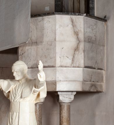 Zdjęcie nr 1: Ambona przyścienna dostępna od strony zakrystii przez kamienny portal o wykroju prostokątnym. Kosz na rzucie połowy ośmioboku wsparty na dwóch kolumnach. Ściany proste, gładkie wyłożone alabastrem, w dolnej części profilowanie, w górnej prosty gzyms wykonany z ciemniejszego kamienia. Kolumny o gładkich, nieco ciemniejszych od struktury ambony trzonach i impostowych kapitelach, wsparte na wspólnej, prostopadłościennej podstawie. W zaplecku portal o prostym, kamiennym obramieniu; w nadprożu płaskorzeźbiony medalion z przedstawieniem gołębicy Ducha Świętego. Drzwi drewniane, polichromowane z efektem marmoryzacji.