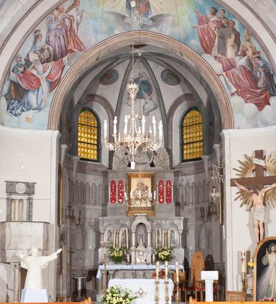 Zdjęcie nr 2: Prezbiterium: 
Sklepienie krzyżowo-żebrowe, dwuprzęsłowe. Pola sklepienne malowane są na kolor beżowy. Od strony wschodniej z centralnie umieszczonymi trzema kolistymi medalionami, mieszczącymi przedstawienie gołębicy Ducha Świętego w obłokach na błękitnym tle (w medalionie centralnym) oraz przeciwstawnie ustawione popiersia dwóch serafinów przedstawionych jako jasnowłosi młodzieńcy w pastelowych szatach, z nimbem wokół głowy (w medalionach skrajnych). W ścianach tarczowych umieszczone wizerunki czterech ewangelistów wraz z ich atrybutami. W pierwszym od wschodu przęśle przedstawienie św. Jana z orłem (po lewej od ołtarza) i św. Mateusza z aniołem (po prawej). W przęśle drugim wizerunek św. Łukasza z uskrzydlonym bykiem (po lewej) i św. Marka z uskrzydlonym lwem (po prawej). Ewangeliści ukazani w popiersiu, na tle błękitnego nieba, obłoków i promienistego nimbu. W dolnej części każdej z kompozycji przedstawione symbole każdego z ewangelistów. Święty Jan ukazany jako młody, jasnowłosy mężczyzna z głową zwróconą w prawo. Ubrany jest w jasnozieloną szatę oraz luźno przerzucony przez ramię różowy płaszcz. W prawym ręku trzyma pióro, w lewym księgę. Świętego Mateusza przedstawiono jako starszego, siwowłosego i brodatego mężczyznę z głową zwróconą w lewo. Ubrany jest w złotą szatę oraz błękitny płaszcz. Swoją lewą rękę składa na piersi, prawą wskazuje w dół. Święty Łukasz przedstawiony jest jako starszy siwowłosy i brodaty mężczyzna ukazany w dynamicznej pozie – z głową z profilu zwróconą w lewo oraz lewą ręką uniesioną do góry. Postać ubrana jest w jasnofioletową szatę oraz błękitny płaszcz. Świętego Marka przedstawiono z ciałem zwróconym w trzech czwartych w prawo i głową ujętą z profilu. Ewangelistę ukazano jako dojrzałego, brodatego mężczyznę o ostrych rysach. Ubrany jest w różową szatę oraz błękitny płaszcz z jasnozieloną podszewką. W swoim prawym ręku trzyma pióro. Elementy architektoniczne takie jak żebra sklepienne, obramienia okien i arkadowych nisz oraz gzyms przebiegający na linii parapetów okiennych są polichromowane w odcieniach szarości z efektem marmoryzacji naśladującej kolorystykę alabastrowych elementów wyposażenia kościoła.
Arkada i ściana tęczowa: Na ścianie tęczowej znajduje się wielopostaciowa, figuralna kompozycja z umieszczonym w centrum przedstawieniem Matki Boskiej Częstochowskiej unoszącej się na skrzydłach orła białego. Przedstawienie to jest flankowane przez dwie grupy świętych. Popiersie Marii z Dzieciątkiem ukazano na tle obłoków oraz promienistej glorii oraz ujęto wieńcem dwunastu gwiazd. Z lewej strony kompozycji ukazano sześcioosobową grupę klęczących świętych, zwracających się w kierunku Marii. Od lewej przedstawiony św. Andrzej Bobola z rękoma skrzyżowanymi na piersi, św. Wojciech w infule i paliuszu szeroko rozpościerający ramiona, św. Kinga w brązowym habicie klaryski z koroną na głowie, błogosławiona Bronisława w jasnoróżowym habicie, z krucyfiksem w dłoni, św. Stanisław biskup i męczennik z pastorałem w dłoni oraz infule na głowie i św. Jadwiga Królowa przedstawiona w złotej koronie i gronostajowym płaszczu. Sześcioosobową grupę świętych ukazanych z prawej strony kompozycji od lewej otwiera postać św. Jana Kantego przedstawionego w birecie oraz obszernym, czerwonym płaszczu z gronostajowym kołnierzem. Za nim przedstawiony św. Stanisław Kostka z rękoma skrzyżowanymi na piersi, następnie św. Jacek w habicie dominikańskim z monstrancją w ręku, błogosławiony Wincenty Kadłubek w stroju biskupim, św. Kazimierz Królewicz w mitrze książęcej oraz czerwonym płaszczu podbitym gronostajem i błogosławiona Salomea przedstawiona w brązowym habicie klaryski, z mitrą na głowie.  
Nawa główna: W nawie sklepienie kolebkowe z lunetami, trójprzęsłowe. Pola sklepienne malowane na kolor jasnobeżowy. W każdym z przęseł, w lunetach sceny figuralne, tworzące cykl ikonograficzny obrazujący sceny z życia Chrystusa i Marii. Wszystkie sceny umieszczone na tle nieba i obłoków. Cykl otwiera scena Zwiastowania umieszczona w pierwszym od prezbiterium przęśle sklepienia po lewej (północnej) stronie. W obłokach ukazani Maria (z prawej) oraz archanioł Gabriel (z lewej), ponad którymi unosi się gołębica Ducha Świętego otoczona świetlistą glorią. Maria przedstawiona jako młoda, jasnowłosa kobieta z ciałem zwróconym w prawo. Głowa otoczona nimbem, pochylona do dołu, prawa ręka złożona na piersi. Postać ubrana jest w białą suknię oraz błękitny płaszcz. Archanioł Gabriel ukazany z profilu w dynamicznej pozie z prawą ręką uniesioną do góry i lewą wyciągniętą do przodu, w której trzyma kwiat lilii. Anioł ubrany jest w długą, jasnoróżową szatę. W kolejnym przęśle przedstawiono Boże Narodzenie. W dolnej części kompozycji ukazani św. Józef (z lewej) i Maria (z prawej) klęczący w obłokach, obok żłóbka z Dzieciątkiem Jezus. Józef ukazany jako dojrzały, brodaty mężczyzna w żółtej szacie i zielonym płaszczu, trzymający w prawej ręce kwiat lilii. Maria przedstawiona jako młoda kobieta z dłońmi złożonymi w geście modlitwy, ubrana w jasnoróżową szatę oraz błękitny płaszcz, którego poła nakrywa jej głowę. Dzieciątko Jezus przepasane białą materią, ukazane frontalnie z rękami wyciągniętymi do góry. W górnej części kompozycji przedstawiony frontalnie długowłosy anioł w jasnozielonej szacie trzymający oburącz banderolę z napisem „GLORIA IN EXCELSIS DEO”. W trzecim przęśle scena Modlitwy w Ogrójcu. Z lewej strony kompozycji przedstawiony z profilu, klęczący Chrystus unoszący do góry ręce złożone w geście modlitwy. Postać ubrana w długą, białą szatę oraz luźno przerzucony przez ramię jasnobłękitny płaszcz. Z prawej strony kompozycji, naprzeciw Chrystusa ukazujący się w obłokach anioł trzymający złoty kielich. Anioł przedstawiony jako długowłosa, młodzieńcza postać ubrana w biało-zielone szaty. Wokół obu postaci rama utworzona z ciemnoszarych, skłębionych obłoków. Kolejne przedstawienia figuralne znajdują się w prawej (południowej) części sklepienia. W pierwszym od strony chóru przęśle przedstawiono Ukrzyżowanie. W centrum kompozycji ukrzyżowany Chrystus z ramionami uniesionymi do góry, tworzącymi linię litery „V”, uniesioną głową w koronie cierniowej oraz stopami przebitymi jednym gwoździem. Postać przepasana długim, białym perizonium. U stóp krzyża ukazani w dynamicznych pozach, z rękoma wzniesionymi do góry św. Jan Ewangelista (z lewej) oraz Maria (z prawej). Święty Jan ubrany w zieloną szatę oraz rozwiany żółto-różowy płaszcz. Maria ukazana w jasnoróżowej sukni oraz granatowo-zielonym płaszczu i chuście na głowie. W kolejnym przęśle przedstawiono scenę Zmartwychwstania. W centrum kompozycji ukazany frontalnie, całopostaciowo zmartwychwstały Chrystus w obszernym, układającym się w dynamicznie załamujące się fałdy, czerwonym płaszczu. Jezus prawą, uniesioną do góry ręką błogosławi, w lewej trzyma chorągiew paschalną. W dolnej części kompozycji przedstawiony anioł w błękitnej szacie podtrzymujący wieko grobowca. W ostatnim przęśle znajduje się scena Wniebowzięcia Marii. W centrum kompozycji, na jasnożółtym tle frontalnie przedstawiona, unosząca się ponad obłokami Maria. Postać ukazana jako młoda kobieta z głową otoczoną wieńcem z gwiazd i rękami uniesionymi do góry. Ubrana jest w jasnoróżową suknię oraz spięty pod szyją, błękitny płaszcz. W dolnej części kompozycji dwa anioły ukazane w dynamicznych pozach. Anioł z lewej strony w zielonej sukni, anioł z prawej w jasnoróżowej. Na ścianie zachodniej kościoła, na wysokości parapetu chóru muzycznego dwie prostokątne płyciny zamknięte łukiem półokrągłym. Płycina z lewej mieści przedstawienie św. Cecylii grającej na organach, płycina z prawej wizerunek króla Dawida grającego na harfie. Pasy gurtów sklepiennych w nawie dekorowane są geometryczną dekoracją z malowanymi pseudopłycinami w kształcie poziomego prostokąta o krótszych bokach zamkniętych łukiem półkolistym z uskokiem. Filary artykułujące nawę, parapet chóru muzycznego oraz gzyms na ścianie zachodniej świątyni polichromowane w odcieniach szarości z efektem marmoryzacji naśladującej kolorystykę alabastrowych elementów wyposażenia kościoła. 
