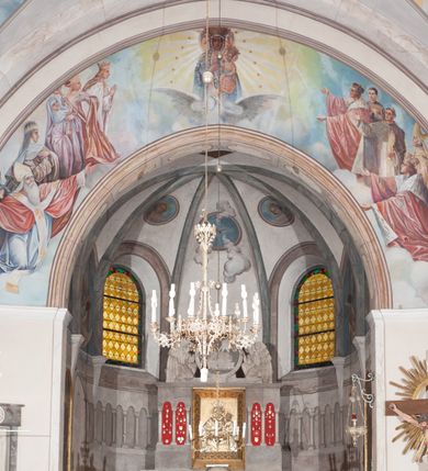 Zdjęcie nr 13: Prezbiterium: 
Sklepienie krzyżowo-żebrowe, dwuprzęsłowe. Pola sklepienne malowane są na kolor beżowy. Od strony wschodniej z centralnie umieszczonymi trzema kolistymi medalionami, mieszczącymi przedstawienie gołębicy Ducha Świętego w obłokach na błękitnym tle (w medalionie centralnym) oraz przeciwstawnie ustawione popiersia dwóch serafinów przedstawionych jako jasnowłosi młodzieńcy w pastelowych szatach, z nimbem wokół głowy (w medalionach skrajnych). W ścianach tarczowych umieszczone wizerunki czterech ewangelistów wraz z ich atrybutami. W pierwszym od wschodu przęśle przedstawienie św. Jana z orłem (po lewej od ołtarza) i św. Mateusza z aniołem (po prawej). W przęśle drugim wizerunek św. Łukasza z uskrzydlonym bykiem (po lewej) i św. Marka z uskrzydlonym lwem (po prawej). Ewangeliści ukazani w popiersiu, na tle błękitnego nieba, obłoków i promienistego nimbu. W dolnej części każdej z kompozycji przedstawione symbole każdego z ewangelistów. Święty Jan ukazany jako młody, jasnowłosy mężczyzna z głową zwróconą w prawo. Ubrany jest w jasnozieloną szatę oraz luźno przerzucony przez ramię różowy płaszcz. W prawym ręku trzyma pióro, w lewym księgę. Świętego Mateusza przedstawiono jako starszego, siwowłosego i brodatego mężczyznę z głową zwróconą w lewo. Ubrany jest w złotą szatę oraz błękitny płaszcz. Swoją lewą rękę składa na piersi, prawą wskazuje w dół. Święty Łukasz przedstawiony jest jako starszy siwowłosy i brodaty mężczyzna ukazany w dynamicznej pozie – z głową z profilu zwróconą w lewo oraz lewą ręką uniesioną do góry. Postać ubrana jest w jasnofioletową szatę oraz błękitny płaszcz. Świętego Marka przedstawiono z ciałem zwróconym w trzech czwartych w prawo i głową ujętą z profilu. Ewangelistę ukazano jako dojrzałego, brodatego mężczyznę o ostrych rysach. Ubrany jest w różową szatę oraz błękitny płaszcz z jasnozieloną podszewką. W swoim prawym ręku trzyma pióro. Elementy architektoniczne takie jak żebra sklepienne, obramienia okien i arkadowych nisz oraz gzyms przebiegający na linii parapetów okiennych są polichromowane w odcieniach szarości z efektem marmoryzacji naśladującej kolorystykę alabastrowych elementów wyposażenia kościoła.
Arkada i ściana tęczowa: Na ścianie tęczowej znajduje się wielopostaciowa, figuralna kompozycja z umieszczonym w centrum przedstawieniem Matki Boskiej Częstochowskiej unoszącej się na skrzydłach orła białego. Przedstawienie to jest flankowane przez dwie grupy świętych. Popiersie Marii z Dzieciątkiem ukazano na tle obłoków oraz promienistej glorii oraz ujęto wieńcem dwunastu gwiazd. Z lewej strony kompozycji ukazano sześcioosobową grupę klęczących świętych, zwracających się w kierunku Marii. Od lewej przedstawiony św. Andrzej Bobola z rękoma skrzyżowanymi na piersi, św. Wojciech w infule i paliuszu szeroko rozpościerający ramiona, św. Kinga w brązowym habicie klaryski z koroną na głowie, błogosławiona Bronisława w jasnoróżowym habicie, z krucyfiksem w dłoni, św. Stanisław biskup i męczennik z pastorałem w dłoni oraz infule na głowie i św. Jadwiga Królowa przedstawiona w złotej koronie i gronostajowym płaszczu. Sześcioosobową grupę świętych ukazanych z prawej strony kompozycji od lewej otwiera postać św. Jana Kantego przedstawionego w birecie oraz obszernym, czerwonym płaszczu z gronostajowym kołnierzem. Za nim przedstawiony św. Stanisław Kostka z rękoma skrzyżowanymi na piersi, następnie św. Jacek w habicie dominikańskim z monstrancją w ręku, błogosławiony Wincenty Kadłubek w stroju biskupim, św. Kazimierz Królewicz w mitrze książęcej oraz czerwonym płaszczu podbitym gronostajem i błogosławiona Salomea przedstawiona w brązowym habicie klaryski, z mitrą na głowie.  
Nawa główna: W nawie sklepienie kolebkowe z lunetami, trójprzęsłowe. Pola sklepienne malowane na kolor jasnobeżowy. W każdym z przęseł, w lunetach sceny figuralne, tworzące cykl ikonograficzny obrazujący sceny z życia Chrystusa i Marii. Wszystkie sceny umieszczone na tle nieba i obłoków. Cykl otwiera scena Zwiastowania umieszczona w pierwszym od prezbiterium przęśle sklepienia po lewej (północnej) stronie. W obłokach ukazani Maria (z prawej) oraz archanioł Gabriel (z lewej), ponad którymi unosi się gołębica Ducha Świętego otoczona świetlistą glorią. Maria przedstawiona jako młoda, jasnowłosa kobieta z ciałem zwróconym w prawo. Głowa otoczona nimbem, pochylona do dołu, prawa ręka złożona na piersi. Postać ubrana jest w białą suknię oraz błękitny płaszcz. Archanioł Gabriel ukazany z profilu w dynamicznej pozie z prawą ręką uniesioną do góry i lewą wyciągniętą do przodu, w której trzyma kwiat lilii. Anioł ubrany jest w długą, jasnoróżową szatę. W kolejnym przęśle przedstawiono Boże Narodzenie. W dolnej części kompozycji ukazani św. Józef (z lewej) i Maria (z prawej) klęczący w obłokach, obok żłóbka z Dzieciątkiem Jezus. Józef ukazany jako dojrzały, brodaty mężczyzna w żółtej szacie i zielonym płaszczu, trzymający w prawej ręce kwiat lilii. Maria przedstawiona jako młoda kobieta z dłońmi złożonymi w geście modlitwy, ubrana w jasnoróżową szatę oraz błękitny płaszcz, którego poła nakrywa jej głowę. Dzieciątko Jezus przepasane białą materią, ukazane frontalnie z rękami wyciągniętymi do góry. W górnej części kompozycji przedstawiony frontalnie długowłosy anioł w jasnozielonej szacie trzymający oburącz banderolę z napisem „GLORIA IN EXCELSIS DEO”. W trzecim przęśle scena Modlitwy w Ogrójcu. Z lewej strony kompozycji przedstawiony z profilu, klęczący Chrystus unoszący do góry ręce złożone w geście modlitwy. Postać ubrana w długą, białą szatę oraz luźno przerzucony przez ramię jasnobłękitny płaszcz. Z prawej strony kompozycji, naprzeciw Chrystusa ukazujący się w obłokach anioł trzymający złoty kielich. Anioł przedstawiony jako długowłosa, młodzieńcza postać ubrana w biało-zielone szaty. Wokół obu postaci rama utworzona z ciemnoszarych, skłębionych obłoków. Kolejne przedstawienia figuralne znajdują się w prawej (południowej) części sklepienia. W pierwszym od strony chóru przęśle przedstawiono Ukrzyżowanie. W centrum kompozycji ukrzyżowany Chrystus z ramionami uniesionymi do góry, tworzącymi linię litery „V”, uniesioną głową w koronie cierniowej oraz stopami przebitymi jednym gwoździem. Postać przepasana długim, białym perizonium. U stóp krzyża ukazani w dynamicznych pozach, z rękoma wzniesionymi do góry św. Jan Ewangelista (z lewej) oraz Maria (z prawej). Święty Jan ubrany w zieloną szatę oraz rozwiany żółto-różowy płaszcz. Maria ukazana w jasnoróżowej sukni oraz granatowo-zielonym płaszczu i chuście na głowie. W kolejnym przęśle przedstawiono scenę Zmartwychwstania. W centrum kompozycji ukazany frontalnie, całopostaciowo zmartwychwstały Chrystus w obszernym, układającym się w dynamicznie załamujące się fałdy, czerwonym płaszczu. Jezus prawą, uniesioną do góry ręką błogosławi, w lewej trzyma chorągiew paschalną. W dolnej części kompozycji przedstawiony anioł w błękitnej szacie podtrzymujący wieko grobowca. W ostatnim przęśle znajduje się scena Wniebowzięcia Marii. W centrum kompozycji, na jasnożółtym tle frontalnie przedstawiona, unosząca się ponad obłokami Maria. Postać ukazana jako młoda kobieta z głową otoczoną wieńcem z gwiazd i rękami uniesionymi do góry. Ubrana jest w jasnoróżową suknię oraz spięty pod szyją, błękitny płaszcz. W dolnej części kompozycji dwa anioły ukazane w dynamicznych pozach. Anioł z lewej strony w zielonej sukni, anioł z prawej w jasnoróżowej. Na ścianie zachodniej kościoła, na wysokości parapetu chóru muzycznego dwie prostokątne płyciny zamknięte łukiem półokrągłym. Płycina z lewej mieści przedstawienie św. Cecylii grającej na organach, płycina z prawej wizerunek króla Dawida grającego na harfie. Pasy gurtów sklepiennych w nawie dekorowane są geometryczną dekoracją z malowanymi pseudopłycinami w kształcie poziomego prostokąta o krótszych bokach zamkniętych łukiem półkolistym z uskokiem. Filary artykułujące nawę, parapet chóru muzycznego oraz gzyms na ścianie zachodniej świątyni polichromowane w odcieniach szarości z efektem marmoryzacji naśladującej kolorystykę alabastrowych elementów wyposażenia kościoła. 
