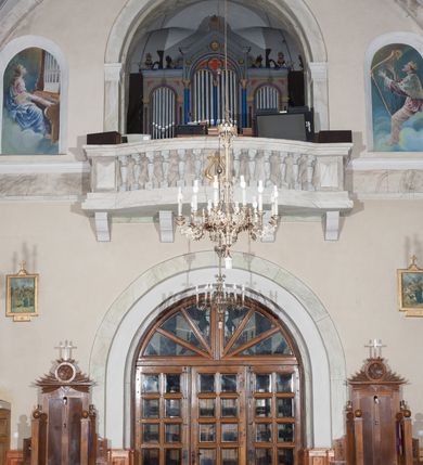 Zdjęcie nr 19: Prezbiterium: 
Sklepienie krzyżowo-żebrowe, dwuprzęsłowe. Pola sklepienne malowane są na kolor beżowy. Od strony wschodniej z centralnie umieszczonymi trzema kolistymi medalionami, mieszczącymi przedstawienie gołębicy Ducha Świętego w obłokach na błękitnym tle (w medalionie centralnym) oraz przeciwstawnie ustawione popiersia dwóch serafinów przedstawionych jako jasnowłosi młodzieńcy w pastelowych szatach, z nimbem wokół głowy (w medalionach skrajnych). W ścianach tarczowych umieszczone wizerunki czterech ewangelistów wraz z ich atrybutami. W pierwszym od wschodu przęśle przedstawienie św. Jana z orłem (po lewej od ołtarza) i św. Mateusza z aniołem (po prawej). W przęśle drugim wizerunek św. Łukasza z uskrzydlonym bykiem (po lewej) i św. Marka z uskrzydlonym lwem (po prawej). Ewangeliści ukazani w popiersiu, na tle błękitnego nieba, obłoków i promienistego nimbu. W dolnej części każdej z kompozycji przedstawione symbole każdego z ewangelistów. Święty Jan ukazany jako młody, jasnowłosy mężczyzna z głową zwróconą w prawo. Ubrany jest w jasnozieloną szatę oraz luźno przerzucony przez ramię różowy płaszcz. W prawym ręku trzyma pióro, w lewym księgę. Świętego Mateusza przedstawiono jako starszego, siwowłosego i brodatego mężczyznę z głową zwróconą w lewo. Ubrany jest w złotą szatę oraz błękitny płaszcz. Swoją lewą rękę składa na piersi, prawą wskazuje w dół. Święty Łukasz przedstawiony jest jako starszy siwowłosy i brodaty mężczyzna ukazany w dynamicznej pozie – z głową z profilu zwróconą w lewo oraz lewą ręką uniesioną do góry. Postać ubrana jest w jasnofioletową szatę oraz błękitny płaszcz. Świętego Marka przedstawiono z ciałem zwróconym w trzech czwartych w prawo i głową ujętą z profilu. Ewangelistę ukazano jako dojrzałego, brodatego mężczyznę o ostrych rysach. Ubrany jest w różową szatę oraz błękitny płaszcz z jasnozieloną podszewką. W swoim prawym ręku trzyma pióro. Elementy architektoniczne takie jak żebra sklepienne, obramienia okien i arkadowych nisz oraz gzyms przebiegający na linii parapetów okiennych są polichromowane w odcieniach szarości z efektem marmoryzacji naśladującej kolorystykę alabastrowych elementów wyposażenia kościoła.
Arkada i ściana tęczowa: Na ścianie tęczowej znajduje się wielopostaciowa, figuralna kompozycja z umieszczonym w centrum przedstawieniem Matki Boskiej Częstochowskiej unoszącej się na skrzydłach orła białego. Przedstawienie to jest flankowane przez dwie grupy świętych. Popiersie Marii z Dzieciątkiem ukazano na tle obłoków oraz promienistej glorii oraz ujęto wieńcem dwunastu gwiazd. Z lewej strony kompozycji ukazano sześcioosobową grupę klęczących świętych, zwracających się w kierunku Marii. Od lewej przedstawiony św. Andrzej Bobola z rękoma skrzyżowanymi na piersi, św. Wojciech w infule i paliuszu szeroko rozpościerający ramiona, św. Kinga w brązowym habicie klaryski z koroną na głowie, błogosławiona Bronisława w jasnoróżowym habicie, z krucyfiksem w dłoni, św. Stanisław biskup i męczennik z pastorałem w dłoni oraz infule na głowie i św. Jadwiga Królowa przedstawiona w złotej koronie i gronostajowym płaszczu. Sześcioosobową grupę świętych ukazanych z prawej strony kompozycji od lewej otwiera postać św. Jana Kantego przedstawionego w birecie oraz obszernym, czerwonym płaszczu z gronostajowym kołnierzem. Za nim przedstawiony św. Stanisław Kostka z rękoma skrzyżowanymi na piersi, następnie św. Jacek w habicie dominikańskim z monstrancją w ręku, błogosławiony Wincenty Kadłubek w stroju biskupim, św. Kazimierz Królewicz w mitrze książęcej oraz czerwonym płaszczu podbitym gronostajem i błogosławiona Salomea przedstawiona w brązowym habicie klaryski, z mitrą na głowie.  
Nawa główna: W nawie sklepienie kolebkowe z lunetami, trójprzęsłowe. Pola sklepienne malowane na kolor jasnobeżowy. W każdym z przęseł, w lunetach sceny figuralne, tworzące cykl ikonograficzny obrazujący sceny z życia Chrystusa i Marii. Wszystkie sceny umieszczone na tle nieba i obłoków. Cykl otwiera scena Zwiastowania umieszczona w pierwszym od prezbiterium przęśle sklepienia po lewej (północnej) stronie. W obłokach ukazani Maria (z prawej) oraz archanioł Gabriel (z lewej), ponad którymi unosi się gołębica Ducha Świętego otoczona świetlistą glorią. Maria przedstawiona jako młoda, jasnowłosa kobieta z ciałem zwróconym w prawo. Głowa otoczona nimbem, pochylona do dołu, prawa ręka złożona na piersi. Postać ubrana jest w białą suknię oraz błękitny płaszcz. Archanioł Gabriel ukazany z profilu w dynamicznej pozie z prawą ręką uniesioną do góry i lewą wyciągniętą do przodu, w której trzyma kwiat lilii. Anioł ubrany jest w długą, jasnoróżową szatę. W kolejnym przęśle przedstawiono Boże Narodzenie. W dolnej części kompozycji ukazani św. Józef (z lewej) i Maria (z prawej) klęczący w obłokach, obok żłóbka z Dzieciątkiem Jezus. Józef ukazany jako dojrzały, brodaty mężczyzna w żółtej szacie i zielonym płaszczu, trzymający w prawej ręce kwiat lilii. Maria przedstawiona jako młoda kobieta z dłońmi złożonymi w geście modlitwy, ubrana w jasnoróżową szatę oraz błękitny płaszcz, którego poła nakrywa jej głowę. Dzieciątko Jezus przepasane białą materią, ukazane frontalnie z rękami wyciągniętymi do góry. W górnej części kompozycji przedstawiony frontalnie długowłosy anioł w jasnozielonej szacie trzymający oburącz banderolę z napisem „GLORIA IN EXCELSIS DEO”. W trzecim przęśle scena Modlitwy w Ogrójcu. Z lewej strony kompozycji przedstawiony z profilu, klęczący Chrystus unoszący do góry ręce złożone w geście modlitwy. Postać ubrana w długą, białą szatę oraz luźno przerzucony przez ramię jasnobłękitny płaszcz. Z prawej strony kompozycji, naprzeciw Chrystusa ukazujący się w obłokach anioł trzymający złoty kielich. Anioł przedstawiony jako długowłosa, młodzieńcza postać ubrana w biało-zielone szaty. Wokół obu postaci rama utworzona z ciemnoszarych, skłębionych obłoków. Kolejne przedstawienia figuralne znajdują się w prawej (południowej) części sklepienia. W pierwszym od strony chóru przęśle przedstawiono Ukrzyżowanie. W centrum kompozycji ukrzyżowany Chrystus z ramionami uniesionymi do góry, tworzącymi linię litery „V”, uniesioną głową w koronie cierniowej oraz stopami przebitymi jednym gwoździem. Postać przepasana długim, białym perizonium. U stóp krzyża ukazani w dynamicznych pozach, z rękoma wzniesionymi do góry św. Jan Ewangelista (z lewej) oraz Maria (z prawej). Święty Jan ubrany w zieloną szatę oraz rozwiany żółto-różowy płaszcz. Maria ukazana w jasnoróżowej sukni oraz granatowo-zielonym płaszczu i chuście na głowie. W kolejnym przęśle przedstawiono scenę Zmartwychwstania. W centrum kompozycji ukazany frontalnie, całopostaciowo zmartwychwstały Chrystus w obszernym, układającym się w dynamicznie załamujące się fałdy, czerwonym płaszczu. Jezus prawą, uniesioną do góry ręką błogosławi, w lewej trzyma chorągiew paschalną. W dolnej części kompozycji przedstawiony anioł w błękitnej szacie podtrzymujący wieko grobowca. W ostatnim przęśle znajduje się scena Wniebowzięcia Marii. W centrum kompozycji, na jasnożółtym tle frontalnie przedstawiona, unosząca się ponad obłokami Maria. Postać ukazana jako młoda kobieta z głową otoczoną wieńcem z gwiazd i rękami uniesionymi do góry. Ubrana jest w jasnoróżową suknię oraz spięty pod szyją, błękitny płaszcz. W dolnej części kompozycji dwa anioły ukazane w dynamicznych pozach. Anioł z lewej strony w zielonej sukni, anioł z prawej w jasnoróżowej. Na ścianie zachodniej kościoła, na wysokości parapetu chóru muzycznego dwie prostokątne płyciny zamknięte łukiem półokrągłym. Płycina z lewej mieści przedstawienie św. Cecylii grającej na organach, płycina z prawej wizerunek króla Dawida grającego na harfie. Pasy gurtów sklepiennych w nawie dekorowane są geometryczną dekoracją z malowanymi pseudopłycinami w kształcie poziomego prostokąta o krótszych bokach zamkniętych łukiem półkolistym z uskokiem. Filary artykułujące nawę, parapet chóru muzycznego oraz gzyms na ścianie zachodniej świątyni polichromowane w odcieniach szarości z efektem marmoryzacji naśladującej kolorystykę alabastrowych elementów wyposażenia kościoła. 
