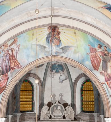 Zdjęcie nr 1: Prezbiterium: 
Sklepienie krzyżowo-żebrowe, dwuprzęsłowe. Pola sklepienne malowane są na kolor beżowy. Od strony wschodniej z centralnie umieszczonymi trzema kolistymi medalionami, mieszczącymi przedstawienie gołębicy Ducha Świętego w obłokach na błękitnym tle (w medalionie centralnym) oraz przeciwstawnie ustawione popiersia dwóch serafinów przedstawionych jako jasnowłosi młodzieńcy w pastelowych szatach, z nimbem wokół głowy (w medalionach skrajnych). W ścianach tarczowych umieszczone wizerunki czterech ewangelistów wraz z ich atrybutami. W pierwszym od wschodu przęśle przedstawienie św. Jana z orłem (po lewej od ołtarza) i św. Mateusza z aniołem (po prawej). W przęśle drugim wizerunek św. Łukasza z uskrzydlonym bykiem (po lewej) i św. Marka z uskrzydlonym lwem (po prawej). Ewangeliści ukazani w popiersiu, na tle błękitnego nieba, obłoków i promienistego nimbu. W dolnej części każdej z kompozycji przedstawione symbole każdego z ewangelistów. Święty Jan ukazany jako młody, jasnowłosy mężczyzna z głową zwróconą w prawo. Ubrany jest w jasnozieloną szatę oraz luźno przerzucony przez ramię różowy płaszcz. W prawym ręku trzyma pióro, w lewym księgę. Świętego Mateusza przedstawiono jako starszego, siwowłosego i brodatego mężczyznę z głową zwróconą w lewo. Ubrany jest w złotą szatę oraz błękitny płaszcz. Swoją lewą rękę składa na piersi, prawą wskazuje w dół. Święty Łukasz przedstawiony jest jako starszy siwowłosy i brodaty mężczyzna ukazany w dynamicznej pozie – z głową z profilu zwróconą w lewo oraz lewą ręką uniesioną do góry. Postać ubrana jest w jasnofioletową szatę oraz błękitny płaszcz. Świętego Marka przedstawiono z ciałem zwróconym w trzech czwartych w prawo i głową ujętą z profilu. Ewangelistę ukazano jako dojrzałego, brodatego mężczyznę o ostrych rysach. Ubrany jest w różową szatę oraz błękitny płaszcz z jasnozieloną podszewką. W swoim prawym ręku trzyma pióro. Elementy architektoniczne takie jak żebra sklepienne, obramienia okien i arkadowych nisz oraz gzyms przebiegający na linii parapetów okiennych są polichromowane w odcieniach szarości z efektem marmoryzacji naśladującej kolorystykę alabastrowych elementów wyposażenia kościoła.
Arkada i ściana tęczowa: Na ścianie tęczowej znajduje się wielopostaciowa, figuralna kompozycja z umieszczonym w centrum przedstawieniem Matki Boskiej Częstochowskiej unoszącej się na skrzydłach orła białego. Przedstawienie to jest flankowane przez dwie grupy świętych. Popiersie Marii z Dzieciątkiem ukazano na tle obłoków oraz promienistej glorii oraz ujęto wieńcem dwunastu gwiazd. Z lewej strony kompozycji ukazano sześcioosobową grupę klęczących świętych, zwracających się w kierunku Marii. Od lewej przedstawiony św. Andrzej Bobola z rękoma skrzyżowanymi na piersi, św. Wojciech w infule i paliuszu szeroko rozpościerający ramiona, św. Kinga w brązowym habicie klaryski z koroną na głowie, błogosławiona Bronisława w jasnoróżowym habicie, z krucyfiksem w dłoni, św. Stanisław biskup i męczennik z pastorałem w dłoni oraz infule na głowie i św. Jadwiga Królowa przedstawiona w złotej koronie i gronostajowym płaszczu. Sześcioosobową grupę świętych ukazanych z prawej strony kompozycji od lewej otwiera postać św. Jana Kantego przedstawionego w birecie oraz obszernym, czerwonym płaszczu z gronostajowym kołnierzem. Za nim przedstawiony św. Stanisław Kostka z rękoma skrzyżowanymi na piersi, następnie św. Jacek w habicie dominikańskim z monstrancją w ręku, błogosławiony Wincenty Kadłubek w stroju biskupim, św. Kazimierz Królewicz w mitrze książęcej oraz czerwonym płaszczu podbitym gronostajem i błogosławiona Salomea przedstawiona w brązowym habicie klaryski, z mitrą na głowie.  
Nawa główna: W nawie sklepienie kolebkowe z lunetami, trójprzęsłowe. Pola sklepienne malowane na kolor jasnobeżowy. W każdym z przęseł, w lunetach sceny figuralne, tworzące cykl ikonograficzny obrazujący sceny z życia Chrystusa i Marii. Wszystkie sceny umieszczone na tle nieba i obłoków. Cykl otwiera scena Zwiastowania umieszczona w pierwszym od prezbiterium przęśle sklepienia po lewej (północnej) stronie. W obłokach ukazani Maria (z prawej) oraz archanioł Gabriel (z lewej), ponad którymi unosi się gołębica Ducha Świętego otoczona świetlistą glorią. Maria przedstawiona jako młoda, jasnowłosa kobieta z ciałem zwróconym w prawo. Głowa otoczona nimbem, pochylona do dołu, prawa ręka złożona na piersi. Postać ubrana jest w białą suknię oraz błękitny płaszcz. Archanioł Gabriel ukazany z profilu w dynamicznej pozie z prawą ręką uniesioną do góry i lewą wyciągniętą do przodu, w której trzyma kwiat lilii. Anioł ubrany jest w długą, jasnoróżową szatę. W kolejnym przęśle przedstawiono Boże Narodzenie. W dolnej części kompozycji ukazani św. Józef (z lewej) i Maria (z prawej) klęczący w obłokach, obok żłóbka z Dzieciątkiem Jezus. Józef ukazany jako dojrzały, brodaty mężczyzna w żółtej szacie i zielonym płaszczu, trzymający w prawej ręce kwiat lilii. Maria przedstawiona jako młoda kobieta z dłońmi złożonymi w geście modlitwy, ubrana w jasnoróżową szatę oraz błękitny płaszcz, którego poła nakrywa jej głowę. Dzieciątko Jezus przepasane białą materią, ukazane frontalnie z rękami wyciągniętymi do góry. W górnej części kompozycji przedstawiony frontalnie długowłosy anioł w jasnozielonej szacie trzymający oburącz banderolę z napisem „GLORIA IN EXCELSIS DEO”. W trzecim przęśle scena Modlitwy w Ogrójcu. Z lewej strony kompozycji przedstawiony z profilu, klęczący Chrystus unoszący do góry ręce złożone w geście modlitwy. Postać ubrana w długą, białą szatę oraz luźno przerzucony przez ramię jasnobłękitny płaszcz. Z prawej strony kompozycji, naprzeciw Chrystusa ukazujący się w obłokach anioł trzymający złoty kielich. Anioł przedstawiony jako długowłosa, młodzieńcza postać ubrana w biało-zielone szaty. Wokół obu postaci rama utworzona z ciemnoszarych, skłębionych obłoków. Kolejne przedstawienia figuralne znajdują się w prawej (południowej) części sklepienia. W pierwszym od strony chóru przęśle przedstawiono Ukrzyżowanie. W centrum kompozycji ukrzyżowany Chrystus z ramionami uniesionymi do góry, tworzącymi linię litery „V”, uniesioną głową w koronie cierniowej oraz stopami przebitymi jednym gwoździem. Postać przepasana długim, białym perizonium. U stóp krzyża ukazani w dynamicznych pozach, z rękoma wzniesionymi do góry św. Jan Ewangelista (z lewej) oraz Maria (z prawej). Święty Jan ubrany w zieloną szatę oraz rozwiany żółto-różowy płaszcz. Maria ukazana w jasnoróżowej sukni oraz granatowo-zielonym płaszczu i chuście na głowie. W kolejnym przęśle przedstawiono scenę Zmartwychwstania. W centrum kompozycji ukazany frontalnie, całopostaciowo zmartwychwstały Chrystus w obszernym, układającym się w dynamicznie załamujące się fałdy, czerwonym płaszczu. Jezus prawą, uniesioną do góry ręką błogosławi, w lewej trzyma chorągiew paschalną. W dolnej części kompozycji przedstawiony anioł w błękitnej szacie podtrzymujący wieko grobowca. W ostatnim przęśle znajduje się scena Wniebowzięcia Marii. W centrum kompozycji, na jasnożółtym tle frontalnie przedstawiona, unosząca się ponad obłokami Maria. Postać ukazana jako młoda kobieta z głową otoczoną wieńcem z gwiazd i rękami uniesionymi do góry. Ubrana jest w jasnoróżową suknię oraz spięty pod szyją, błękitny płaszcz. W dolnej części kompozycji dwa anioły ukazane w dynamicznych pozach. Anioł z lewej strony w zielonej sukni, anioł z prawej w jasnoróżowej. Na ścianie zachodniej kościoła, na wysokości parapetu chóru muzycznego dwie prostokątne płyciny zamknięte łukiem półokrągłym. Płycina z lewej mieści przedstawienie św. Cecylii grającej na organach, płycina z prawej wizerunek króla Dawida grającego na harfie. Pasy gurtów sklepiennych w nawie dekorowane są geometryczną dekoracją z malowanymi pseudopłycinami w kształcie poziomego prostokąta o krótszych bokach zamkniętych łukiem półkolistym z uskokiem. Filary artykułujące nawę, parapet chóru muzycznego oraz gzyms na ścianie zachodniej świątyni polichromowane w odcieniach szarości z efektem marmoryzacji naśladującej kolorystykę alabastrowych elementów wyposażenia kościoła. 
