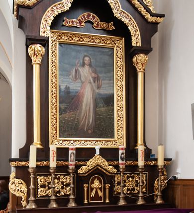 Zdjęcie nr 1: Nastawa ołtarzowa architektoniczna, jednoosiowa, jednokondygnacyjna, ustawiona na niskim cokole. Ołtarz drewniany, prostopadłościenny. Mensa drewniana. Antepedium w formie leżącego prostokąta zdobione dwiema płycinami w kształcie stojących prostokątów, dekorowanymi w polu stylizowaną wicią roślinną i jedną kwadratową pośrodku z krzyżem w polu. Tabernakulum wmontowane w cokół, delikatnie wysunięte do przodu, flankowane dwiema kolumienkami wspierającymi niepełne belkowanie, zamknięte łukiem ostrym i ozdobione u szczytu bujną, płaskorzeźbioną wicią stylizowanego akantu. Drzwiczki w kształcie stojącego prostokąta zamknięte łukiem półkolistym z płaskorzeźbionym gorejącym sercem, owiniętym koroną cierniową z krzyżykiem i odchodzącymi od niego dwoma promieniami. Kondygnacja ujęta dwiema smukłymi kolumnami wspierającymi niepełne belkowanie. W polu głównym obraz Jezusa Miłosiernego umieszczony w szerokiej ramie. Nad obrazem wstęga z napisem „JEZU UFAM TOBIE” na czerwonym tle. Zwieńczenie w formie baldachimu, nad polem głównym wykrojonego trójlistnie, od góry zamkniętego łukiem ostrym. Szczyt zdobiony płaskorzeźbioną, ażurową, stylizowaną wicią akantu i łacińskim krzyżykiem pośrodku. Struktura w kolorze naturalnego drewna; ornamentyka złocona, detale czerwone. 




