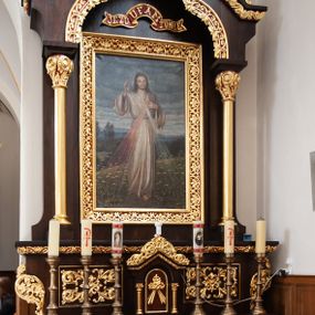 Zdjęcie nr 1: Nastawa ołtarzowa architektoniczna, jednoosiowa, jednokondygnacyjna, ustawiona na niskim cokole. Ołtarz drewniany, prostopadłościenny. Mensa drewniana. Antepedium w formie leżącego prostokąta zdobione dwiema płycinami w kształcie stojących prostokątów, dekorowanymi w polu stylizowaną wicią roślinną i jedną kwadratową pośrodku z krzyżem w polu. Tabernakulum wmontowane w cokół, delikatnie wysunięte do przodu, flankowane dwiema kolumienkami wspierającymi niepełne belkowanie, zamknięte łukiem ostrym i ozdobione u szczytu bujną, płaskorzeźbioną wicią stylizowanego akantu. Drzwiczki w kształcie stojącego prostokąta zamknięte łukiem półkolistym z płaskorzeźbionym gorejącym sercem, owiniętym koroną cierniową z krzyżykiem i odchodzącymi od niego dwoma promieniami. Kondygnacja ujęta dwiema smukłymi kolumnami wspierającymi niepełne belkowanie. W polu głównym obraz Jezusa Miłosiernego umieszczony w szerokiej ramie. Nad obrazem wstęga z napisem „JEZU UFAM TOBIE” na czerwonym tle. Zwieńczenie w formie baldachimu, nad polem głównym wykrojonego trójlistnie, od góry zamkniętego łukiem ostrym. Szczyt zdobiony płaskorzeźbioną, ażurową, stylizowaną wicią akantu i łacińskim krzyżykiem pośrodku. Struktura w kolorze naturalnego drewna; ornamentyka złocona, detale czerwone. 




