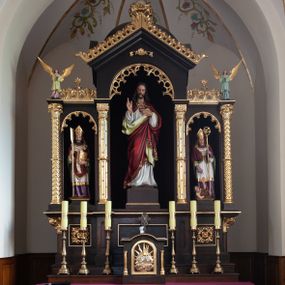 Zdjęcie nr 1: Nastawa ołtarzowa architektoniczna, trójosiowa, jednokondygnacyjna, na wysokim cokole. Ołtarz drewniany, prostopadłościenny; mensa drewniana. Antepedium w formie leżącego prostokąta ujęte w narożach kolumienkami, w polu trzy prostokątne płyciny, w środkowej monogram IHS na czerwonym tle otoczony promienistą glorią. Tabernakulum w formie prostopadłościennej skrzynki, ustawione na wysokim cokole, flankowane dwiem kolumienkami, zamknięte od góry gzymsem w kształcie łuku nadwieszonego. Drzwiczki w kształcie stojącego prostokąta, zamkniętego łukiem półkolistym, w polu płaskorzeźbione przedstawienie baranka paschalnego. Cokół nastawy trójosiowy, oś środkowa wydzielona pilastrami, na skrajach osi bocznych ćwierćkolumny z kapitelami w formie liści akantu. W polach osi bocznych kwadratowe płyciny wypełnione rozetami, w osi środkowej płycina w kształcie leżącego prostokąta. Cokół podtrzymuje nastawę, flankowaną dwiema parami kolumn, z których środkowe podtrzymują kopułę z przyczółkiem, a kolumny boczne figury aniołów. We wnęce środkowej figura Najświętszego Serca Jezusa, we wnęce lewej św. Wojciech, a po prawej św. Stanisław. Kolumny ustawione na bazach, przedzielone w połowie opaską, o trzonach zdobionych geometrycznymi motywami i kapitelach dekorowanych liśćmi akantu. U szczytu przyczółka duży kwiaton z zatkniętym krzyżem osadzonym na kuli. Gzymsy zdobione ażurową dekoracją roślinną. Łuki wnęk dekorowane arkadowaniami, w tym środkowa z maswerkami. Ponadto szczyt osi środkowej oraz gzyms nad osiami bocznymi wieńczy ornamentalny krenelaż. Struktura malowana w kolorze ciemnego brązu, ornamentyka i detale złocone. 

