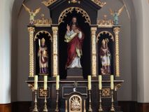 Zdjęcie nr 1: Nastawa ołtarzowa architektoniczna, trójosiowa, jednokondygnacyjna, na wysokim cokole. Ołtarz drewniany, prostopadłościenny; mensa drewniana. Antepedium w formie leżącego prostokąta ujęte w narożach kolumienkami, w polu trzy prostokątne płyciny, w środkowej monogram IHS na czerwonym tle otoczony promienistą glorią. Tabernakulum w formie prostopadłościennej skrzynki, ustawione na wysokim cokole, flankowane dwiem kolumienkami, zamknięte od góry gzymsem w kształcie łuku nadwieszonego. Drzwiczki w kształcie stojącego prostokąta, zamkniętego łukiem półkolistym, w polu płaskorzeźbione przedstawienie baranka paschalnego. Cokół nastawy trójosiowy, oś środkowa wydzielona pilastrami, na skrajach osi bocznych ćwierćkolumny z kapitelami w formie liści akantu. W polach osi bocznych kwadratowe płyciny wypełnione rozetami, w osi środkowej płycina w kształcie leżącego prostokąta. Cokół podtrzymuje nastawę, flankowaną dwiema parami kolumn, z których środkowe podtrzymują kopułę z przyczółkiem, a kolumny boczne figury aniołów. We wnęce środkowej figura Najświętszego Serca Jezusa, we wnęce lewej św. Wojciech, a po prawej św. Stanisław. Kolumny ustawione na bazach, przedzielone w połowie opaską, o trzonach zdobionych geometrycznymi motywami i kapitelach dekorowanych liśćmi akantu. U szczytu przyczółka duży kwiaton z zatkniętym krzyżem osadzonym na kuli. Gzymsy zdobione ażurową dekoracją roślinną. Łuki wnęk dekorowane arkadowaniami, w tym środkowa z maswerkami. Ponadto szczyt osi środkowej oraz gzyms nad osiami bocznymi wieńczy ornamentalny krenelaż. Struktura malowana w kolorze ciemnego brązu, ornamentyka i detale złocone. 

