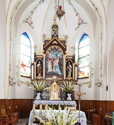 Zdjęcie nr 2: Nastawa ołtarzowa architektoniczna, trójosiowa, jednokondygnacyjna ze zwieńczeniem, na wysokim cokole. Ołtarz drewniany, prostopadłościenny; mensa drewniana. Antepedium w formie leżącego prostokąta ujęte w narożach półkolumienkami, w polu płaskorzeźbione przedstawienie Ostatniej Wieczerzy. Cokół retabulum z czterema pilastrami, stanowiącymi podstawę dla podpór. Osie wydzielone dwiema parami kolumn; środkowe wyższe od bocznych. W polu środkowym głęboka nisza z płaskorzeźbionym przedstawieniem Nawiedzenia Najświętszej Marii Panny i w formie stojącego prostokąta zamkniętego łukiem półkolistym, ujęta parą kolumn o kapitelach kompozytowych; arkada zamknięta trójkątnym szczytem, flankowanym wspornikami z figurkami aniołów; za nim fragment dachu. Osie boczne niższe, z niszami na figury św. Piotra i św. Pawła w formie stojącego prostokąta zamkniętego łukiem półkolistym; od zewnątrz ujęte półkolumienkami o kapitelach korynckich dźwigających fryz i postumenty dla figurek aniołów. Kondygnacja ujęta przyporami. Zwieńczenie w formie ośmiobocznego baldachimu opartego na arkadkach z figurą św. Michała Archanioła. Na szczycie łaciński krzyż o trójlistnie zakończonych ramionach. Na osiach zewnętrznych cokołu prześwity wypełnione wicią roślinną z motywem winnego grona. Cokół zakończony pasem z dekoracją roślinną. Trzony wewnętrznej pary kolumn dekorowane kratką z rozetami, w połowie wysokości ujęte koroną. Trzony zewnętrznej pary podpór zdobione ornamentem geometryczno-roślinnym. Łuki nisz dekorowane stylizowanym maswerkiem; pole szczytu rozetą, gzyms stylizowanymi żabkami. Osie boczne zwieńczone palmetami z rozetą. Kalenica dachu z ciągiem palmet.
Struktura w kolorze naturalnego drewna; ornamentyka i podpory złocone i srebrzone.