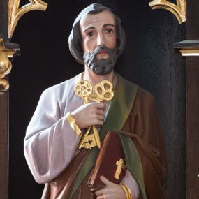 Zdjęcie nr 1: Rzeźba św. Piotra ustawiona na niskim prostopadłościennym cokole o ściętych narożach. Święty Piotr ukazany frontalnie, w delikatnym kontrapoście, z lewą nogą ugiętą w kolanie. W prawej dłoni trzyma dwa skrzyżowane klucze, a w lewej księgę. Twarz podłużna ze zmarszczonym czołem, z długim i szerokim nosem, dużymi oczami i małymi ustami, okolona średniej długości brodą. Włosy ciemnobrązowe, gęste i zasłaniające uszy. Ubrany jest w długą fioletową suknię z długimi rękawami oraz brązowy płaszcz z zieloną podszewką, zdobiony na brzegach dekoracyjnym pasem utworzonym z ukośnych kresek. Księga w czerwonej obwolucie, zdobiona złotym, łacińskim krzyżykiem. Polichromia w odsłoniętych partiach ciała naturalistyczna, detale złocone.