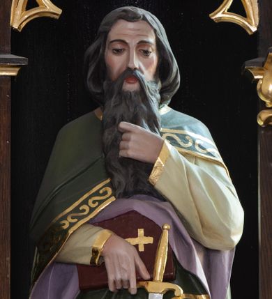 Zdjęcie nr 1: Rzeźba św. Pawła ustawiona na niskim prostopadłościennym cokole, o ściętych narożach. Święty Paweł ukazany jest frontalnie, w delikatnym kontrapoście, z prawą nogą ugiętą w kolanie. W prawej dłoni trzyma księgę oraz miecz, lewą dotyka długiej brody. Twarz o czerwonej karnacji z długim i szerokim nosem, wzrokiem spuszczonym w dół, okolona długą i bujną brodą. Włosy ciemnobrązowe, gęste i zasłaniające uszy. Ubrany jest w beżową suknię z długimi rękawami oraz zielony płaszcz z fioletową podszewką, zdobiony na brzegach dekoracyjnym pasem utworzonym z malowanych na złoto esownic. Księga w czerwonej obwolucie, zdobiona złotym krzyżykiem. Polichromia w odsłoniętych partiach ciała naturalistyczna, detale złocone.