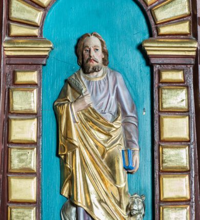 Zdjęcie nr 4: Ambona drewniana, przyścienna, dostępna jednobiegowymi schodkami od strony prezbiterium. Kosz na planie ośmioboku, na cokole dekorowanym złoconym ornamentem małżowinowym; artykułowany pilastrami wspierającymi fryz wypełniony złoconym ornamentem małżowinowym. Na trzonach pilastrów złocony ornament kwiatowy podwieszony na wstędze regencyjnej. W polach płyciny ujęte boniowanymi arkadkami mieszczącymi płaskorzeźbione, całopostaciowe przedstawienia ewangelistów na niebieskim tle. Całość zwieńczona profilowanym gzymsem. Zaplecek z półkolistą niszą mieszczącą płaskorzeźbione przedstawienie Chrystusa Dobrego Pasterza, ujętą pilastrami dźwigającymi niepełne belkowanie. Na trzonach podwieszone złocone zwisy kwiatowe przewiązane karbowaną wstęgą. Baldachim ośmioboczny z silnie występującym, profilowanym gzymsem. W podniebiu płaskorzeźbione przedstawienie gołębicy Ducha Świętego. W zwieńczeniu, na ośmiobocznym postumencie wolnostojąca, pełnoplastyczna rzeźba anioła grającego na trąbie. Figury ewangelistów ukazane frontalnie, w postawie stojącej, w dłoniach z których jedna jest złożona na piersi, trzymają pióra oraz zwoje lub księgi. Mają twarze podłużne, okolone brodami i średniej długości włosami. W pierwszej arkadzie od lewej strony ukazany jest św. Mateusz z małą postacią człowieka u nóg. Święty ubrany jest w brązową suknię oraz złoty płaszcz; ma siwe włosy. W kolejnej arkadzie św. Marek, a za nim lew. Święty ubrany jest w fioletową suknię i złocony płaszcz. W następnej arkadzie św. Łukasz, obok którego wyłania się wół. Ubrany jest w niebieską suknię i złocony płaszcz; ma siwe włosy i brodę. W ostatniej arkadzie ukazano św. Jana z orłem u stóp, ubranego w zieloną suknię i złocony płaszcz, bez zarostu, z długimi i jasnymi włosami. Chrystus ukazany frontalnie z barankiem założonym na barku, przytrzymujący go lewą ręką, z kijem pasterskim w prawej dłoni i drugim barankiem u stóp. Twarz podłużna o głęboko osadzonych, dużych oczach, okolona krótką brodą i długimi włosami. U szczytu anioł grający na trąbie. Ubrany jest w jasnofioletową suknię oraz krótką złoconą tunikę. Struktura malowana na ciemny brąz, partie ornamentu złocone.