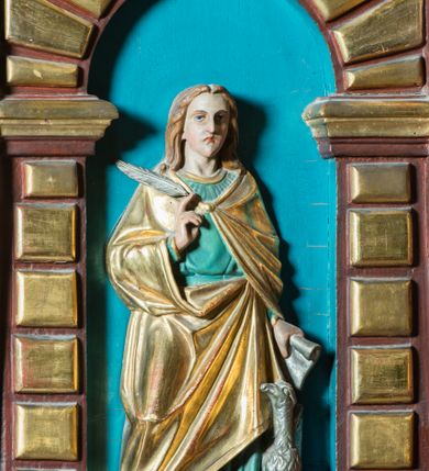 Zdjęcie nr 5: Ambona drewniana, przyścienna, dostępna jednobiegowymi schodkami od strony prezbiterium. Kosz na planie ośmioboku, na cokole dekorowanym złoconym ornamentem małżowinowym; artykułowany pilastrami wspierającymi fryz wypełniony złoconym ornamentem małżowinowym. Na trzonach pilastrów złocony ornament kwiatowy podwieszony na wstędze regencyjnej. W polach płyciny ujęte boniowanymi arkadkami mieszczącymi płaskorzeźbione, całopostaciowe przedstawienia ewangelistów na niebieskim tle. Całość zwieńczona profilowanym gzymsem. Zaplecek z półkolistą niszą mieszczącą płaskorzeźbione przedstawienie Chrystusa Dobrego Pasterza, ujętą pilastrami dźwigającymi niepełne belkowanie. Na trzonach podwieszone złocone zwisy kwiatowe przewiązane karbowaną wstęgą. Baldachim ośmioboczny z silnie występującym, profilowanym gzymsem. W podniebiu płaskorzeźbione przedstawienie gołębicy Ducha Świętego. W zwieńczeniu, na ośmiobocznym postumencie wolnostojąca, pełnoplastyczna rzeźba anioła grającego na trąbie. Figury ewangelistów ukazane frontalnie, w postawie stojącej, w dłoniach z których jedna jest złożona na piersi, trzymają pióra oraz zwoje lub księgi. Mają twarze podłużne, okolone brodami i średniej długości włosami. W pierwszej arkadzie od lewej strony ukazany jest św. Mateusz z małą postacią człowieka u nóg. Święty ubrany jest w brązową suknię oraz złoty płaszcz; ma siwe włosy. W kolejnej arkadzie św. Marek, a za nim lew. Święty ubrany jest w fioletową suknię i złocony płaszcz. W następnej arkadzie św. Łukasz, obok którego wyłania się wół. Ubrany jest w niebieską suknię i złocony płaszcz; ma siwe włosy i brodę. W ostatniej arkadzie ukazano św. Jana z orłem u stóp, ubranego w zieloną suknię i złocony płaszcz, bez zarostu, z długimi i jasnymi włosami. Chrystus ukazany frontalnie z barankiem założonym na barku, przytrzymujący go lewą ręką, z kijem pasterskim w prawej dłoni i drugim barankiem u stóp. Twarz podłużna o głęboko osadzonych, dużych oczach, okolona krótką brodą i długimi włosami. U szczytu anioł grający na trąbie. Ubrany jest w jasnofioletową suknię oraz krótką złoconą tunikę. Struktura malowana na ciemny brąz, partie ornamentu złocone.