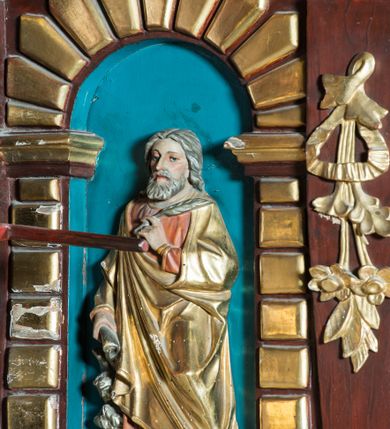 Zdjęcie nr 6: Ambona drewniana, przyścienna, dostępna jednobiegowymi schodkami od strony prezbiterium. Kosz na planie ośmioboku, na cokole dekorowanym złoconym ornamentem małżowinowym; artykułowany pilastrami wspierającymi fryz wypełniony złoconym ornamentem małżowinowym. Na trzonach pilastrów złocony ornament kwiatowy podwieszony na wstędze regencyjnej. W polach płyciny ujęte boniowanymi arkadkami mieszczącymi płaskorzeźbione, całopostaciowe przedstawienia ewangelistów na niebieskim tle. Całość zwieńczona profilowanym gzymsem. Zaplecek z półkolistą niszą mieszczącą płaskorzeźbione przedstawienie Chrystusa Dobrego Pasterza, ujętą pilastrami dźwigającymi niepełne belkowanie. Na trzonach podwieszone złocone zwisy kwiatowe przewiązane karbowaną wstęgą. Baldachim ośmioboczny z silnie występującym, profilowanym gzymsem. W podniebiu płaskorzeźbione przedstawienie gołębicy Ducha Świętego. W zwieńczeniu, na ośmiobocznym postumencie wolnostojąca, pełnoplastyczna rzeźba anioła grającego na trąbie. Figury ewangelistów ukazane frontalnie, w postawie stojącej, w dłoniach z których jedna jest złożona na piersi, trzymają pióra oraz zwoje lub księgi. Mają twarze podłużne, okolone brodami i średniej długości włosami. W pierwszej arkadzie od lewej strony ukazany jest św. Mateusz z małą postacią człowieka u nóg. Święty ubrany jest w brązową suknię oraz złoty płaszcz; ma siwe włosy. W kolejnej arkadzie św. Marek, a za nim lew. Święty ubrany jest w fioletową suknię i złocony płaszcz. W następnej arkadzie św. Łukasz, obok którego wyłania się wół. Ubrany jest w niebieską suknię i złocony płaszcz; ma siwe włosy i brodę. W ostatniej arkadzie ukazano św. Jana z orłem u stóp, ubranego w zieloną suknię i złocony płaszcz, bez zarostu, z długimi i jasnymi włosami. Chrystus ukazany frontalnie z barankiem założonym na barku, przytrzymujący go lewą ręką, z kijem pasterskim w prawej dłoni i drugim barankiem u stóp. Twarz podłużna o głęboko osadzonych, dużych oczach, okolona krótką brodą i długimi włosami. U szczytu anioł grający na trąbie. Ubrany jest w jasnofioletową suknię oraz krótką złoconą tunikę. Struktura malowana na ciemny brąz, partie ornamentu złocone.