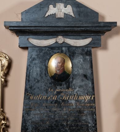 Zdjęcie nr 1: Nagrobek w formie steli zwężającej się nieznacznie ku górze, zakończonej gzymsem zdobionym festonem spiętym rozetą. Nad gzymsem cokół o ściętych narożach zdobiony uskrzydloną klepsydrą i zwieńczony amforą. W górnej części steli owalny portret zmarłego ukazanego w trzech czwartych, w prawo. Jego twarz jest szczupła, z wyraźnie zaznaczonymi łukami brwiowymi, wysokim czołem, uwypuklonymi kośćmi policzkowymi, prostym, długi, nosem. Oczy ma zwrócone na wprost, a usta zaciśnięte. Włosy jasne, krótkie, po bokach głowy. Ubrany w granatowy mundur, zapinany na trzy złote guzy z czerwoną stójką i koronkowym żabotem. Popiersie na blaszanym tle. Poniżej portretu inskrypcja:  "Na pamiątkę / Mateusza Kirchmajer / Syna Józefa i Maryanny z Bartschów Kirchmajerów, / Obywatela i Sędziego Pokoju Rzeczypospolitej Krakowskiej, / zmarłego bezżennie w 55 roku życia swojego, / dnia 8go sierpnia 1831 lata, / Pozostałe Rodzeństwo w dowód przywiązania, / pomnik ten w roku 1834 położyło. / Usługi dla Dobra Kraju podjęte, prace w Towarzystwach dobroczyn/nych, przeznaczona ostatnią wolą część majątku na wsparcie nędzy, / przekazały następnym wdzięczną pamięć i jego cnót i zasług. / Zwłoki spoczywają w grobie rodzinnym Kościoła tego, / Duch złączony z Bogiem, w Bogu spoczywa"