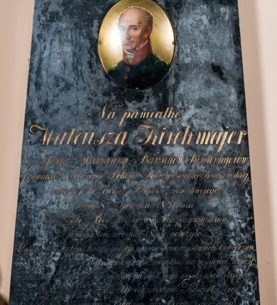 Zdjęcie nr 2: Nagrobek w formie steli zwężającej się nieznacznie ku górze, zakończonej gzymsem zdobionym festonem spiętym rozetą. Nad gzymsem cokół o ściętych narożach zdobiony uskrzydloną klepsydrą i zwieńczony amforą. W górnej części steli owalny portret zmarłego ukazanego w trzech czwartych, w prawo. Jego twarz jest szczupła, z wyraźnie zaznaczonymi łukami brwiowymi, wysokim czołem, uwypuklonymi kośćmi policzkowymi, prostym, długi, nosem. Oczy ma zwrócone na wprost, a usta zaciśnięte. Włosy jasne, krótkie, po bokach głowy. Ubrany w granatowy mundur, zapinany na trzy złote guzy z czerwoną stójką i koronkowym żabotem. Popiersie na blaszanym tle. Poniżej portretu inskrypcja:  &quot;Na pamiątkę / Mateusza Kirchmajer / Syna Józefa i Maryanny z Bartschów Kirchmajerów, / Obywatela i Sędziego Pokoju Rzeczypospolitej Krakowskiej, / zmarłego bezżennie w 55 roku życia swojego, / dnia 8go sierpnia 1831 lata, / Pozostałe Rodzeństwo w dowód przywiązania, / pomnik ten w roku 1834 położyło. / Usługi dla Dobra Kraju podjęte, prace w Towarzystwach dobroczyn/nych, przeznaczona ostatnią wolą część majątku na wsparcie nędzy, / przekazały następnym wdzięczną pamięć i jego cnót i zasług. / Zwłoki spoczywają w grobie rodzinnym Kościoła tego, / Duch złączony z Bogiem, w Bogu spoczywa&quot;