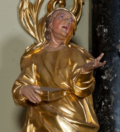 Zdjęcie nr 1: Rzeźba ścięta z tyłu, drążona, ustawiona na niskiej podstawie. Figura stojąca, w kontrapoście, zwrócona frontalnie z głową przechyloną na lewe ramię, skierowaną ku górze. Jej lewa ręka jest wyciągnięta przed siebie, a w prawej dłoni trzyma księgę opartą na biodrze. Twarz ascetyczna, o starczych rysach, głęboko osadzone oczy z silnie uwypuklonymi brwiami, nos niewielki, usta lekko rozchylone, podbródek wydatny. Włosy długie, delikatnie kręcone, opadają na ramiona. Święta jest ubrana w suknię o wąskich, drapowanych rękawach, przepasaną w talii oraz płaszcz, przewiązany w partii bioder, opadający na prawy bok, długi, odsłaniający fragmenty stóp. Na głowie ściśle do niej przylegający welon. Polichromia naturalistyczna w odsłoniętych partiach ciała. Szaty i atrybut złocony.