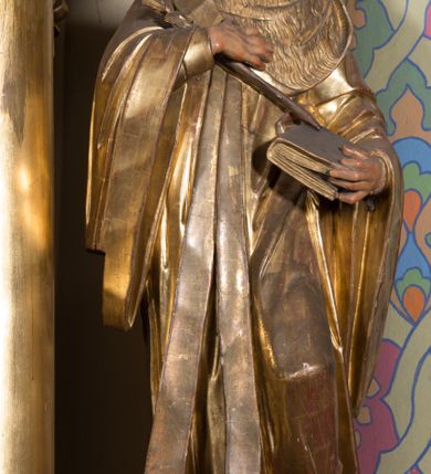 Zdjęcie nr 4: Rzeźba ścięta z tyłu, drążona, ustawiona na prostopadłościennej niskiej podstawie. Postać ukazana w kontrapoście, frontalnie, z głową skierowaną w prawo. Prawą ręką przytrzymuje na piersi kwiat lilii, w lewej zamkniętą księgę. Jego twarz jest ascetyczna, nos krótki z wgłębieniem nad nim, o głęboko rzeźbionych rysach, wyraźnie zaznaczonych brwiach wysoko uniesionych, widocznych zmarszczkach wzdłuż policzków, wąskich i szeroko otwartych oczach, ustach pełnych, nieznacznie rozchylonych. Twarz okolona krótką, szpiczastą, kręconą brodą. Włosy krótkie, rzeźbione w pojedyncze pukle opadające na tył głowy. Święty jest ubrany w tunikę, togę profesorską z szerokimi rękawami, rozchyloną na przodzie, ściśle przylegającą do ciała, swobodnie drapowaną w pojedyncze fałdy, odpowiadające układowi ciała, z gronostajowym kołnierzem na piersi. 
Polichromia naturalistyczna w odsłoniętych partiach ciała; szaty i atrybuty złocone.