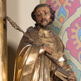 Zdjęcie nr 1: Rzeźba ścięta z tyłu, drążona, ustawiona na prostopadłościennej niskiej podstawie. Postać ukazana w kontrapoście, frontalnie, z głową skierowaną w prawo. Prawą ręką przytrzymuje na piersi kwiat lilii, w lewej zamkniętą księgę. Jego twarz jest ascetyczna, nos krótki z wgłębieniem nad nim, o głęboko rzeźbionych rysach, wyraźnie zaznaczonych brwiach wysoko uniesionych, widocznych zmarszczkach wzdłuż policzków, wąskich i szeroko otwartych oczach, ustach pełnych, nieznacznie rozchylonych. Twarz okolona krótką, szpiczastą, kręconą brodą. Włosy krótkie, rzeźbione w pojedyncze pukle opadające na tył głowy. Święty jest ubrany w tunikę, togę profesorską z szerokimi rękawami, rozchyloną na przodzie, ściśle przylegającą do ciała, swobodnie drapowaną w pojedyncze fałdy, odpowiadające układowi ciała, z gronostajowym kołnierzem na piersi. 
Polichromia naturalistyczna w odsłoniętych partiach ciała; szaty i atrybuty złocone.