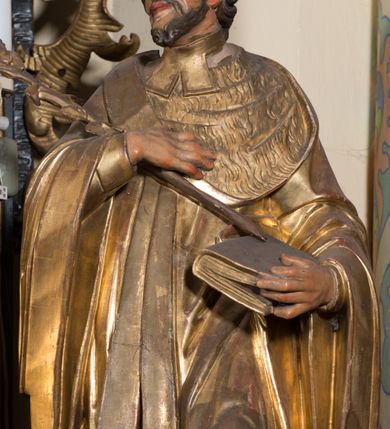 Zdjęcie nr 2: Rzeźba ścięta z tyłu, drążona, ustawiona na prostopadłościennej niskiej podstawie. Postać ukazana w kontrapoście, frontalnie, z głową skierowaną w prawo. Prawą ręką przytrzymuje na piersi kwiat lilii, w lewej zamkniętą księgę. Jego twarz jest ascetyczna, nos krótki z wgłębieniem nad nim, o głęboko rzeźbionych rysach, wyraźnie zaznaczonych brwiach wysoko uniesionych, widocznych zmarszczkach wzdłuż policzków, wąskich i szeroko otwartych oczach, ustach pełnych, nieznacznie rozchylonych. Twarz okolona krótką, szpiczastą, kręconą brodą. Włosy krótkie, rzeźbione w pojedyncze pukle opadające na tył głowy. Święty jest ubrany w tunikę, togę profesorską z szerokimi rękawami, rozchyloną na przodzie, ściśle przylegającą do ciała, swobodnie drapowaną w pojedyncze fałdy, odpowiadające układowi ciała, z gronostajowym kołnierzem na piersi. 
Polichromia naturalistyczna w odsłoniętych partiach ciała; szaty i atrybuty złocone.