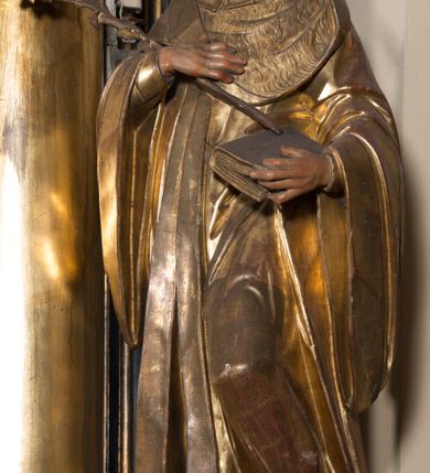 Zdjęcie nr 5: Rzeźba ścięta z tyłu, drążona, ustawiona na prostopadłościennej niskiej podstawie. Postać ukazana w kontrapoście, frontalnie, z głową skierowaną w prawo. Prawą ręką przytrzymuje na piersi kwiat lilii, w lewej zamkniętą księgę. Jego twarz jest ascetyczna, nos krótki z wgłębieniem nad nim, o głęboko rzeźbionych rysach, wyraźnie zaznaczonych brwiach wysoko uniesionych, widocznych zmarszczkach wzdłuż policzków, wąskich i szeroko otwartych oczach, ustach pełnych, nieznacznie rozchylonych. Twarz okolona krótką, szpiczastą, kręconą brodą. Włosy krótkie, rzeźbione w pojedyncze pukle opadające na tył głowy. Święty jest ubrany w tunikę, togę profesorską z szerokimi rękawami, rozchyloną na przodzie, ściśle przylegającą do ciała, swobodnie drapowaną w pojedyncze fałdy, odpowiadające układowi ciała, z gronostajowym kołnierzem na piersi. 
Polichromia naturalistyczna w odsłoniętych partiach ciała; szaty i atrybuty złocone.