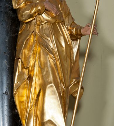 Zdjęcie nr 5: Rzeźba ścięta z tyłu, drążona, ustawiona na niskiej podstawie. Figura zwrócona w trzech czwartych w lewo, z głową ukazaną frontalnie, lekko przechyloną na prawe ramię. Święty stoi w kontrapoście, delikatnie przechylając się do tyłu. Jego prawa ręka spoczywa na piersi, a w lewej odchylonej od ciała trzyma wiosło. Jego twarz jest szczupła, o wyraźnie podkreślonych i wygiętych łukach brwiowych, oczy głęboko osadzone, spoglądające ku górze, nos krótki, szeroki, usta pełne i delikatnie rozchylone. Twarz okala długa broda, opadająca faliście na pierś. Włosy kręcone, formowane w osobne pukle, ekspresyjnie rozwiane. Święty jest ubrany w długą szatę o wąskich rękawach, przepasaną w talii, ściśle przylegającą do ciała w partii torsu, układającą się w ostre fałdy u dołu. Polichromia naturalistyczna w odsłoniętych partiach ciała, szaty i atrybut złocony.