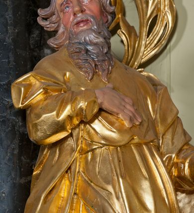 Zdjęcie nr 6: Rzeźba ścięta z tyłu, drążona, ustawiona na niskiej podstawie. Figura zwrócona w trzech czwartych w lewo, z głową ukazaną frontalnie, lekko przechyloną na prawe ramię. Święty stoi w kontrapoście, delikatnie przechylając się do tyłu. Jego prawa ręka spoczywa na piersi, a w lewej odchylonej od ciała trzyma wiosło. Jego twarz jest szczupła, o wyraźnie podkreślonych i wygiętych łukach brwiowych, oczy głęboko osadzone, spoglądające ku górze, nos krótki, szeroki, usta pełne i delikatnie rozchylone. Twarz okala długa broda, opadająca faliście na pierś. Włosy kręcone, formowane w osobne pukle, ekspresyjnie rozwiane. Święty jest ubrany w długą szatę o wąskich rękawach, przepasaną w talii, ściśle przylegającą do ciała w partii torsu, układającą się w ostre fałdy u dołu. Polichromia naturalistyczna w odsłoniętych partiach ciała, szaty i atrybut złocony.