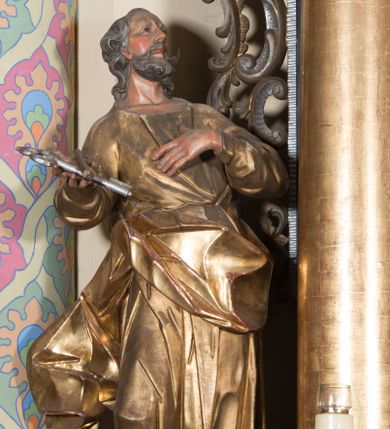 Zdjęcie nr 1: Rzeźba ścięta z tyłu, drążona, ustawiona na prostokątnej podstawie. Figura zwrócona frontalnie, z głową skierowaną w lewo, uniesiona do góry. Ciało ukazane w kontrapoście, przechylone w tył. Święty lewą rękę kładzie na piersi, w prawej wysuniętej do przodu trzyma skrzyżowane klucze. Jego twarz jest ascetyczna o ostrych rysach, głęboko osadzonych oczach o trójkątnych, wysoko uniesionych powiekach, nos ma niewielki, okrągły, a usta delikatnie rozchylone z widocznym podniebieniem. Twarz okolona krótką brodą, układającą się w dwa pukle. Włosy kręcone, głęboko rzeźbione, opadające na tył szyi. Święty jest ubrany w tunikę o wąskich drapowanych rękawach, ściśle przylegającą do ciała w partii torsu oraz obficie drapowaną i delikatnie łamaną w dolnej części. Płaszcz przewiązany przez biodra z rozwianym zwisem na prawym boku. Polichromia naturalistyczna w odsłoniętych partiach ciała, szaty złocone, klucze srebrzone.