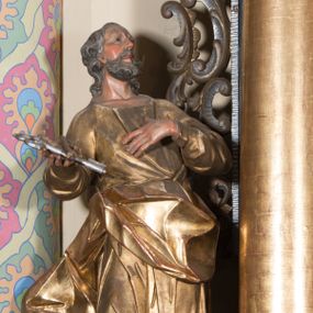 Zdjęcie nr 1: Rzeźba ścięta z tyłu, drążona, ustawiona na prostokątnej podstawie. Figura zwrócona frontalnie, z głową skierowaną w lewo, uniesiona do góry. Ciało ukazane w kontrapoście, przechylone w tył. Święty lewą rękę kładzie na piersi, w prawej wysuniętej do przodu trzyma skrzyżowane klucze. Jego twarz jest ascetyczna o ostrych rysach, głęboko osadzonych oczach o trójkątnych, wysoko uniesionych powiekach, nos ma niewielki, okrągły, a usta delikatnie rozchylone z widocznym podniebieniem. Twarz okolona krótką brodą, układającą się w dwa pukle. Włosy kręcone, głęboko rzeźbione, opadające na tył szyi. Święty jest ubrany w tunikę o wąskich drapowanych rękawach, ściśle przylegającą do ciała w partii torsu oraz obficie drapowaną i delikatnie łamaną w dolnej części. Płaszcz przewiązany przez biodra z rozwianym zwisem na prawym boku. Polichromia naturalistyczna w odsłoniętych partiach ciała, szaty złocone, klucze srebrzone.