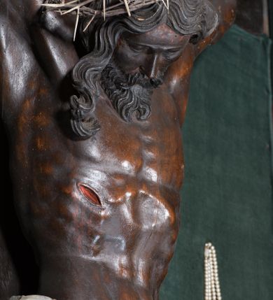 Zdjęcie nr 4: Chrystus ukazany w typie christo morte, w silnym zwisie, z głową opadającą na prawe ramię, nogami delikatnie ugiętymi w kolanach i skrzyżowanymi stopami przebitymi jednym gwoździem. Twarz pociągła, szczupła o wyraźnie zaznaczonych kościach policzkowych i długim nosie, z zamkniętymi oczami. Twarz okolona krótką, falowaną brodą. Włosy falowane, długie opadające na prawie ramię. Ciało szczupłe, o wyraźnie zarysowanej muskulaturze i klatce piersiowej. Perizonium gęsto drapowane w drobne fałdki, ściśle opinające biodra, przewiązane po prawej stronie, ze zwisem tkaniny sięgającym kolan.  Na górnej belce krzyża titulus w formie kartusza, z dekoracją małżowinową oraz napisem "INRI". Ciało polichromowane na brązowo, szaty złocone.