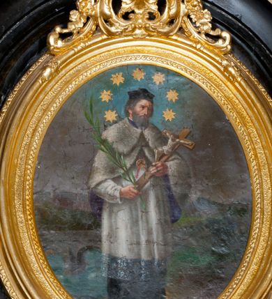 Zdjęcie nr 1: Obraz w formie stojącego owalu, w drewnianej, złoconej, profilowanej ramie, u szczytu dekorowanej ornamentem roślinnym. W centrum przedstawienie stojącego św. Jana Nepomucena, zwróconego w trzech czwartych w lewo, z krucyfiksem i palmą męczeństwa w dłoniach. Jego głowa jest delikatnie pochylona, twarz okolona krótką brodą, włosy krótkie. Jest ubrany w sutannę i komżę, almucję zapinaną na piersi, opadającą na ramiona oraz biret na głowie. Wokół głowy świetlisty nimb z siedmioma gwiazdami. Święty jest przedstawiony na tle mostu Karola w Pradze i architektonicznego pejzażu miejskiego, nad którym szaro-niebieskie niebo. 