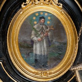 Zdjęcie nr 1: Obraz w formie stojącego owalu, w drewnianej, złoconej, profilowanej ramie, u szczytu dekorowanej ornamentem roślinnym. W centrum przedstawienie stojącego św. Jana Nepomucena, zwróconego w trzech czwartych w lewo, z krucyfiksem i palmą męczeństwa w dłoniach. Jego głowa jest delikatnie pochylona, twarz okolona krótką brodą, włosy krótkie. Jest ubrany w sutannę i komżę, almucję zapinaną na piersi, opadającą na ramiona oraz biret na głowie. Wokół głowy świetlisty nimb z siedmioma gwiazdami. Święty jest przedstawiony na tle mostu Karola w Pradze i architektonicznego pejzażu miejskiego, nad którym szaro-niebieskie niebo. 