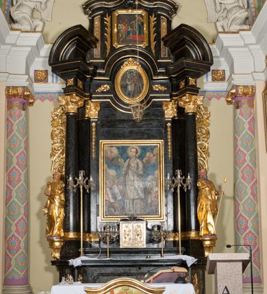 Zdjęcie nr 3: Ołtarz jednoosiowy, jednokondygnacyjny ze zwieńczeniem. Mensa marmurowa, antepedium z płyciną w kształcie leżącego prostokąta o ściętych ćwierćkoliście narożach oraz drewnianym i płaskorzeźbionym przedstawieniem Baranka Eucharystycznego leżącego na księdze, na obłoku, w glorii. Nastawa ujęta parą stojących na ukośnie dostawionych postumentach kolumn kompozytowych na tle zwielokrotnionych pilastrów, dźwigających pełne belkowanie z wydatnym gzymsem, wyłamane na osi podpór oraz przerwany półkolisty przyczółek. Belkowanie rozerwane owalnym polem z obrazem ukazującym św. Jana Nepomucena. Po zewnętrznej stronie podpór figury św. Anny i św. Joachima na wydatnych wspornikach. W polu środkowym profilowana rama w formie stojącego prostokąta z obrazem św. Wawrzyńca. Zwieńczenie w formie stojącego prostokąta, ujęte zdwojonymi pilastrami; zamknięte gzymsem przyjmującym kształt łuku w ośli grzbiet zakończonego stylizowaną palmetą. W polu profilowana rama w formie stojącego prostokąta o ściętych narożach z obrazem „Ofiarowanie Marii do świątyni”. Trzony pilastrów dekorowane kampanulami. Imposty dekorowane z trzech stron rozetami, fryz nad polem środkowym retabulum akantem. Kondygnacja ujęta uszami utworzonymi z suchego akantu z motywem słonecznika. Trzony pilastrów zwieńczenia dekorowane płycinami z kampanulami. Pole obrazowe flankowane liśćmi palmowymi, zwieńczone kamienną muszlą. Na gzymsie zwieńczenia umieszczono festony. Ornamentyka, profilowania i kapitele kolumn są złocone.