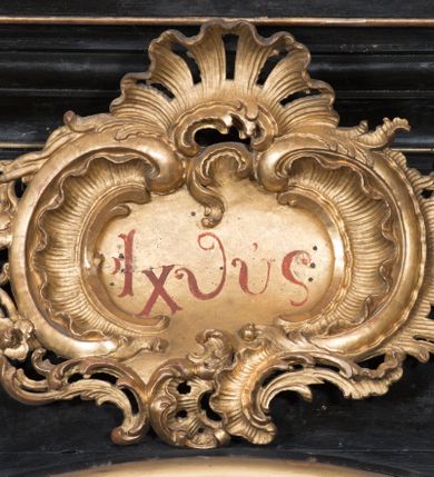 Zdjęcie nr 8: Ołtarz architektoniczny, jednoosiowy, jednokondygnacyjny ze zwieńczeniem. Ołtarz drewniany prostopadłościenny, mensa drewniana z portatylem z marmuru dębnickiego. W ołtarzu nisza z Grobem Pańskim, zakryta antepedium dekorowanym ramą w formie leżącego prostokąta o wklęsłych narożach z monogramem IHS w polu. Na ściankach bocznych ołtarza płyciny w formie kwadratu o wklęsłych narożach. Retabulum jest ujęte parą kompozytowych kolumn ustawionych na ukośnych cokołach stojących, na tle zwielokrotnionych pilastrów o kanelowanych trzonach, dźwigających pełne belkowanie z wydatnym gzymsem wyłamane na osi podpór oraz przerwany półkolisty przyczółek z figurami siedzących puttów; architraw nad polem środkowym przybiera kształt łuku odcinkowego. Po zewnętrznej stronie kolumn figury św. Piotra i św. Pawła stojące na wydatnych konsolach. W polu środkowym nisza ujęta profilowaną ramą w formie stojącego prostokąta zamkniętego łukiem odcinkowym nadwieszonym z figurą Chrystusa Ukrzyżowanego. Zwieńczenie w formie stojącego prostokąta ujęte zwielokrotnionymi pilastrami podtrzymującymi profilowany gzyms przyjmujący kształt łuku oślego. W polu owalne pole z obrazem „Zesłanie Ducha Świętego”. Cokoły dekorowane płycinami utworzonymi z ornamentu roślinnego, zaś konsole zdobione muszlą o kształcie falbany. Nad polem środkowym rocaille&#039;owy kartusz z napisem: „IXEUS”, flankowany akantem. U spodu obrazu prostokątna płycina. Fryz zdobiony rozetami. Kondygnacja ujęta ażurowymi uszami utworzonymi z suchego akantu, wstęgi, rocaille&#039;u i rozet. Trzony pilastrów zwieńczenia dekorowane rocaille&#039;em i roślinnymi festonami. Pole obrazowe otoczone fragmentami rocaille&#039;u, zwieńczone muszlą. Ponad zwieńczeniem krzyż lub wazon nakryty sukienką na puszkę. Struktura polichromowana w kolorze czarnym; kolumny, ornamentyka i profile złocone.