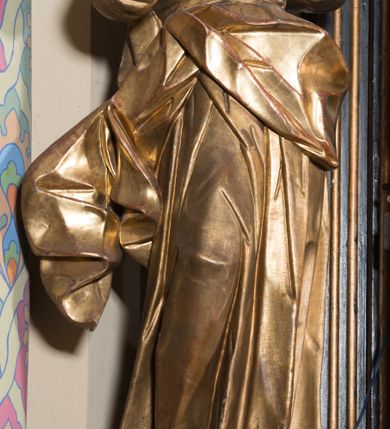 Zdjęcie nr 26: Ołtarz architektoniczny, jednoosiowy, jednokondygnacyjny ze zwieńczeniem. Ołtarz drewniany prostopadłościenny, mensa drewniana z portatylem z marmuru dębnickiego. W ołtarzu nisza z Grobem Pańskim, zakryta antepedium dekorowanym ramą w formie leżącego prostokąta o wklęsłych narożach z monogramem IHS w polu. Na ściankach bocznych ołtarza płyciny w formie kwadratu o wklęsłych narożach. Retabulum jest ujęte parą kompozytowych kolumn ustawionych na ukośnych cokołach stojących, na tle zwielokrotnionych pilastrów o kanelowanych trzonach, dźwigających pełne belkowanie z wydatnym gzymsem wyłamane na osi podpór oraz przerwany półkolisty przyczółek z figurami siedzących puttów; architraw nad polem środkowym przybiera kształt łuku odcinkowego. Po zewnętrznej stronie kolumn figury św. Piotra i św. Pawła stojące na wydatnych konsolach. W polu środkowym nisza ujęta profilowaną ramą w formie stojącego prostokąta zamkniętego łukiem odcinkowym nadwieszonym z figurą Chrystusa Ukrzyżowanego. Zwieńczenie w formie stojącego prostokąta ujęte zwielokrotnionymi pilastrami podtrzymującymi profilowany gzyms przyjmujący kształt łuku oślego. W polu owalne pole z obrazem „Zesłanie Ducha Świętego”. Cokoły dekorowane płycinami utworzonymi z ornamentu roślinnego, zaś konsole zdobione muszlą o kształcie falbany. Nad polem środkowym rocaille&#039;owy kartusz z napisem: „IXEUS”, flankowany akantem. U spodu obrazu prostokątna płycina. Fryz zdobiony rozetami. Kondygnacja ujęta ażurowymi uszami utworzonymi z suchego akantu, wstęgi, rocaille&#039;u i rozet. Trzony pilastrów zwieńczenia dekorowane rocaille&#039;em i roślinnymi festonami. Pole obrazowe otoczone fragmentami rocaille&#039;u, zwieńczone muszlą. Ponad zwieńczeniem krzyż lub wazon nakryty sukienką na puszkę. Struktura polichromowana w kolorze czarnym; kolumny, ornamentyka i profile złocone.