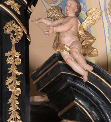 Zdjęcie nr 7: Ołtarz architektoniczny, jednoosiowy, jednokondygnacyjny ze zwieńczeniem. Ołtarz drewniany prostopadłościenny, mensa drewniana z portatylem z marmuru dębnickiego. W ołtarzu nisza z Grobem Pańskim, zakryta antepedium dekorowanym ramą w formie leżącego prostokąta o wklęsłych narożach z monogramem IHS w polu. Na ściankach bocznych ołtarza płyciny w formie kwadratu o wklęsłych narożach. Retabulum jest ujęte parą kompozytowych kolumn ustawionych na ukośnych cokołach stojących, na tle zwielokrotnionych pilastrów o kanelowanych trzonach, dźwigających pełne belkowanie z wydatnym gzymsem wyłamane na osi podpór oraz przerwany półkolisty przyczółek z figurami siedzących puttów; architraw nad polem środkowym przybiera kształt łuku odcinkowego. Po zewnętrznej stronie kolumn figury św. Piotra i św. Pawła stojące na wydatnych konsolach. W polu środkowym nisza ujęta profilowaną ramą w formie stojącego prostokąta zamkniętego łukiem odcinkowym nadwieszonym z figurą Chrystusa Ukrzyżowanego. Zwieńczenie w formie stojącego prostokąta ujęte zwielokrotnionymi pilastrami podtrzymującymi profilowany gzyms przyjmujący kształt łuku oślego. W polu owalne pole z obrazem „Zesłanie Ducha Świętego”. Cokoły dekorowane płycinami utworzonymi z ornamentu roślinnego, zaś konsole zdobione muszlą o kształcie falbany. Nad polem środkowym rocaille'owy kartusz z napisem: „IXEUS”, flankowany akantem. U spodu obrazu prostokątna płycina. Fryz zdobiony rozetami. Kondygnacja ujęta ażurowymi uszami utworzonymi z suchego akantu, wstęgi, rocaille'u i rozet. Trzony pilastrów zwieńczenia dekorowane rocaille'em i roślinnymi festonami. Pole obrazowe otoczone fragmentami rocaille'u, zwieńczone muszlą. Ponad zwieńczeniem krzyż lub wazon nakryty sukienką na puszkę. Struktura polichromowana w kolorze czarnym; kolumny, ornamentyka i profile złocone.