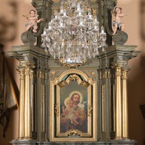 Zdjęcie nr 1: Nastawa architektoniczna, jednokondygnacyjna, jednoosiowa ze zwieńczeniem. Ołtarz sarkofagowy, wybrzuszony, z drewnianą mensą i drewnianym portatylem integralnie zespolony z cokołem retabulum. Nastawa wsparta na ukośnie ustawionych postumentach z filarami i stojącymi przed nimi oraz z boku wolnostojącymi kolumnami z głowicami akantowymi, podtrzymującymi wspólnie, wznoszące się nad nimi belkowanie. Zwieńczenie ujęte ukośnie posadowionymi spływami wolutowymi podtrzymującymi gzyms wyłamujący się pośrodku łukowato. W środku nastawy głęboka wnęka w profilowanym obramieniu z motywem skręconego sznura, prostokątna o ściętych górą narożach, zamknięta łukiem półkolistym nadwieszonym. W niej obraz przedstawiający św. Józefa z Dzieciątkiem, w ramie powielającej wykrój wnęki, z drobnymi rocaille'ami na bokach. W zwieńczeniu wnęka prostokątna w profilowanym obramieniu, z motywem skręconego sznura, ujęta po bokach kłosami zbóż, a zwieńczona motywem akantu. W niej obraz prostokątny obraz z wyobrażeniem św. Stanisława Kostki. Na spływach wolutowych uskrzydlone nagie aniołki z przepaską na biodrach. Nad wnęką w środkowej części ołtarza wypukły kartusz ujęty rocaile'm, drobne rocaille nad wnęką i na filarach, w partii cokołu utworzona z motywu rocaille'owego konsola.  Kolorystyka  struktury w odcieniu  zieleni wpadającej w szarość, partie detalu architektonicznego i ornamentyka  złocone.