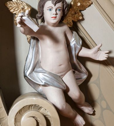 Zdjęcie nr 6: Ambona nadwieszona z dostępem w postaci jednobiegowych schodów usytuowanych z prawej strony kosza. Kosz na rzucie półkolistym, z podwieszoną szyszką u spodu. Ścianki kosza flankowane dwoma spływami wolutowymi. Cokół kosza zaakcentowany szeregiem form przypominających obłoki. Ścianki kosza podzielone na sześć  pionowych, prostokątnych, o wciętych półkoliście krótszych bokach, wypełnionych dekoracją z motywów rocaille. Gzyms profilowany, przełamany na osi spływów. Na wolutach spływów oraz pośrodku kosza osadzone trzy figury aniołków. Zaplecek rozszerzający się ku dołowi, flankowany parą spływów; w jego polu obraz w kształcie pionowego prostokąta zamkniętego łukiem wklęsło-wypukłym z przedstawieniem św. Jana Nepomucena. Zaplecek ujęty z boków i zwieńczony spiętą kotarą z frędzlami. Baldachim na planie analogicznym jak kosz, o wysokim, profilowanym dolnym brzegu, obwiedziony od dołu lambrekinem z frędzlami. W polu podniebienia baldachimu gołębica Ducha Świętego na tle promienistej glorii, z przodu na brzegu baldachimu kartusz z motywu rocaille. Podniebienie baldachimu w kolorze niebieskim, na polu gołębica Ducha Świętego na tle promienistej glorii, z przodu rocaille'owy kartusz. Szczyt baldachimu w formie wysokiego postumentu, na którym ustawiona rzeźba Michała Archanioła zwyciężającego szatana. Po bokach postumentu dwa rzeźbione aniołki. Święty Michał Archanioł ukazany w pozycji stojącej o esowato wygiętej sylwetce, z prawą ręką uniesioną wysoko ku górze, w której trzyma płomienisty miecz, w lewej owalna tarcza z monogramem Chrystusa i trzema gwoździami, lewą stopą depcze leżącego szatana. Ubrany w strój legionisty rzymskiego, skrzydła złocone, szeroko rozłożone. Szatan ukazany w monstrualnej postaci, w pozycji leżącej na brzuchu, z lewą nogą uniesioną wysoko ku górze. Postać polichromowana na czarno, detale (oczy, usta, rogi, paznokcie) na czerwono. Aniołki ukazane w poruszonych pozach, przepasane srebrną chustką, z szeroko rozłożonymi złoconymi skrzydłami. Balustrada schodów zamknięta od dołu cokołem i od góry profilowanym gzymsem, zdobiona w polu romboidalną płyciną, zakończona słupkiem z wazonem płomienistym na szczycie. Struktura ambony polichromowana na kolor jasno i ciemnobeżowy, detale i płyciny na kolor niebieski, ornamentyka złocona.
