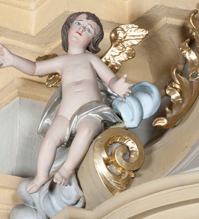 Zdjęcie nr 8: Ambona nadwieszona z dostępem w postaci jednobiegowych schodów usytuowanych z prawej strony kosza. Kosz na rzucie półkolistym, z podwieszoną szyszką u spodu. Ścianki kosza flankowane dwoma spływami wolutowymi. Cokół kosza zaakcentowany szeregiem form przypominających obłoki. Ścianki kosza podzielone na sześć  pionowych, prostokątnych, o wciętych półkoliście krótszych bokach, wypełnionych dekoracją z motywów rocaille. Gzyms profilowany, przełamany na osi spływów. Na wolutach spływów oraz pośrodku kosza osadzone trzy figury aniołków. Zaplecek rozszerzający się ku dołowi, flankowany parą spływów; w jego polu obraz w kształcie pionowego prostokąta zamkniętego łukiem wklęsło-wypukłym z przedstawieniem św. Jana Nepomucena. Zaplecek ujęty z boków i zwieńczony spiętą kotarą z frędzlami. Baldachim na planie analogicznym jak kosz, o wysokim, profilowanym dolnym brzegu, obwiedziony od dołu lambrekinem z frędzlami. W polu podniebienia baldachimu gołębica Ducha Świętego na tle promienistej glorii, z przodu na brzegu baldachimu kartusz z motywu rocaille. Podniebienie baldachimu w kolorze niebieskim, na polu gołębica Ducha Świętego na tle promienistej glorii, z przodu rocaille&#039;owy kartusz. Szczyt baldachimu w formie wysokiego postumentu, na którym ustawiona rzeźba Michała Archanioła zwyciężającego szatana. Po bokach postumentu dwa rzeźbione aniołki. Święty Michał Archanioł ukazany w pozycji stojącej o esowato wygiętej sylwetce, z prawą ręką uniesioną wysoko ku górze, w której trzyma płomienisty miecz, w lewej owalna tarcza z monogramem Chrystusa i trzema gwoździami, lewą stopą depcze leżącego szatana. Ubrany w strój legionisty rzymskiego, skrzydła złocone, szeroko rozłożone. Szatan ukazany w monstrualnej postaci, w pozycji leżącej na brzuchu, z lewą nogą uniesioną wysoko ku górze. Postać polichromowana na czarno, detale (oczy, usta, rogi, paznokcie) na czerwono. Aniołki ukazane w poruszonych pozach, przepasane srebrną chustką, z szeroko rozłożonymi złoconymi skrzydłami. Balustrada schodów zamknięta od dołu cokołem i od góry profilowanym gzymsem, zdobiona w polu romboidalną płyciną, zakończona słupkiem z wazonem płomienistym na szczycie. Struktura ambony polichromowana na kolor jasno i ciemnobeżowy, detale i płyciny na kolor niebieski, ornamentyka złocona.
