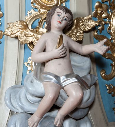 Zdjęcie nr 5: Ambona nadwieszona z dostępem w postaci jednobiegowych schodów usytuowanych z prawej strony kosza. Kosz na rzucie półkolistym, z podwieszoną szyszką u spodu. Ścianki kosza flankowane dwoma spływami wolutowymi. Cokół kosza zaakcentowany szeregiem form przypominających obłoki. Ścianki kosza podzielone na sześć  pionowych, prostokątnych, o wciętych półkoliście krótszych bokach, wypełnionych dekoracją z motywów rocaille. Gzyms profilowany, przełamany na osi spływów. Na wolutach spływów oraz pośrodku kosza osadzone trzy figury aniołków. Zaplecek rozszerzający się ku dołowi, flankowany parą spływów; w jego polu obraz w kształcie pionowego prostokąta zamkniętego łukiem wklęsło-wypukłym z przedstawieniem św. Jana Nepomucena. Zaplecek ujęty z boków i zwieńczony spiętą kotarą z frędzlami. Baldachim na planie analogicznym jak kosz, o wysokim, profilowanym dolnym brzegu, obwiedziony od dołu lambrekinem z frędzlami. W polu podniebienia baldachimu gołębica Ducha Świętego na tle promienistej glorii, z przodu na brzegu baldachimu kartusz z motywu rocaille. Podniebienie baldachimu w kolorze niebieskim, na polu gołębica Ducha Świętego na tle promienistej glorii, z przodu rocaille'owy kartusz. Szczyt baldachimu w formie wysokiego postumentu, na którym ustawiona rzeźba Michała Archanioła zwyciężającego szatana. Po bokach postumentu dwa rzeźbione aniołki. Święty Michał Archanioł ukazany w pozycji stojącej o esowato wygiętej sylwetce, z prawą ręką uniesioną wysoko ku górze, w której trzyma płomienisty miecz, w lewej owalna tarcza z monogramem Chrystusa i trzema gwoździami, lewą stopą depcze leżącego szatana. Ubrany w strój legionisty rzymskiego, skrzydła złocone, szeroko rozłożone. Szatan ukazany w monstrualnej postaci, w pozycji leżącej na brzuchu, z lewą nogą uniesioną wysoko ku górze. Postać polichromowana na czarno, detale (oczy, usta, rogi, paznokcie) na czerwono. Aniołki ukazane w poruszonych pozach, przepasane srebrną chustką, z szeroko rozłożonymi złoconymi skrzydłami. Balustrada schodów zamknięta od dołu cokołem i od góry profilowanym gzymsem, zdobiona w polu romboidalną płyciną, zakończona słupkiem z wazonem płomienistym na szczycie. Struktura ambony polichromowana na kolor jasno i ciemnobeżowy, detale i płyciny na kolor niebieski, ornamentyka złocona.
