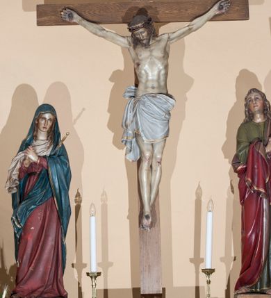 Zdjęcie nr 1: Grupa Ukrzyżowania składa się z: krucyfiksu, figury Matki Bożej po lewej oraz św. Jana Ewangelisty po prawej stronie. Wszystkie rzeźby są pełnoplastyczne ustawione na jednym dużym, schodkowym cokole. Chrystus zawieszony na silnie wyprężonych ramionach, prawa noga założona na lewą, przybite do krzyża jednym gwoździem; głowa przechylona na prawe ramię. Twarz podłużna z zamkniętymi oczami, długi i wąski nos. Na głowie korona cierniowa, spod której na plecy i prawe ramię spływają kręcone włosy. Perizonium białe, na brzegu zdobione podwójną złotą lamówką, przewiązane podwójnym sznurem, z jednym końcem zwisającym wzdłuż prawego uda. Nad głową Chrystusa titulus w formie poziomej banderoli z napisem „INRI”. Krzyż gładki i prosty. Matka Boska  ukazana frontalnie, w postawie stojącej z rękami złożonymi w geście „affectus doloris” przy prawym ramieniu, jej serce przebija sztylet, głowa delikatnie skłoniona w dół. Twarz szeroka, z długim i wąskim nosem, oczy wpatrzone w dal, włosy długie, spływające na ramiona. Ubrana jest w czerwoną suknię przewiązaną brązowym paskiem oraz niebieski płaszcz założony na głowę i przerzucony przez lewe ramię, wokół szyi biała chusta. Po drugiej stronie rzeźba św. Jana ustawiona analogicznie jak rzeźba Matki Boskiej, z głową skierowaną ku górze. Twarz o młodzieńczych rysach, z oczami skierowanymi na Chrystusa, nos długi i wąski, włosy długie, opadające na ramiona i plecy. Święty jest ubrany w zieloną suknię z długimi rękawami oraz czerwony płaszcz zarzucony na plecy i lewe ramię. Szaty Marii i św. Jana obwiedzione na brzegach podwójną, złotą lamówką. Polichromie w odsłoniętych partiach ciała naturalistyczne. Cokół wysoki, profilowany, w górnej partii rozdzielony na trzy mniejsze postumenty pod każdą z figur. Cokół w kolorze jasnozielonym zdobiony złotą, stylizowaną wicią roślinną. 


