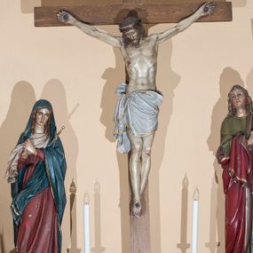 Zdjęcie nr 1: Grupa Ukrzyżowania składa się z: krucyfiksu, figury Matki Bożej po lewej oraz św. Jana Ewangelisty po prawej stronie. Wszystkie rzeźby są pełnoplastyczne ustawione na jednym dużym, schodkowym cokole. Chrystus zawieszony na silnie wyprężonych ramionach, prawa noga założona na lewą, przybite do krzyża jednym gwoździem; głowa przechylona na prawe ramię. Twarz podłużna z zamkniętymi oczami, długi i wąski nos. Na głowie korona cierniowa, spod której na plecy i prawe ramię spływają kręcone włosy. Perizonium białe, na brzegu zdobione podwójną złotą lamówką, przewiązane podwójnym sznurem, z jednym końcem zwisającym wzdłuż prawego uda. Nad głową Chrystusa titulus w formie poziomej banderoli z napisem „INRI”. Krzyż gładki i prosty. Matka Boska  ukazana frontalnie, w postawie stojącej z rękami złożonymi w geście „affectus doloris” przy prawym ramieniu, jej serce przebija sztylet, głowa delikatnie skłoniona w dół. Twarz szeroka, z długim i wąskim nosem, oczy wpatrzone w dal, włosy długie, spływające na ramiona. Ubrana jest w czerwoną suknię przewiązaną brązowym paskiem oraz niebieski płaszcz założony na głowę i przerzucony przez lewe ramię, wokół szyi biała chusta. Po drugiej stronie rzeźba św. Jana ustawiona analogicznie jak rzeźba Matki Boskiej, z głową skierowaną ku górze. Twarz o młodzieńczych rysach, z oczami skierowanymi na Chrystusa, nos długi i wąski, włosy długie, opadające na ramiona i plecy. Święty jest ubrany w zieloną suknię z długimi rękawami oraz czerwony płaszcz zarzucony na plecy i lewe ramię. Szaty Marii i św. Jana obwiedzione na brzegach podwójną, złotą lamówką. Polichromie w odsłoniętych partiach ciała naturalistyczne. Cokół wysoki, profilowany, w górnej partii rozdzielony na trzy mniejsze postumenty pod każdą z figur. Cokół w kolorze jasnozielonym zdobiony złotą, stylizowaną wicią roślinną. 



