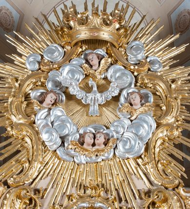 Zdjęcie nr 2: Ołtarz jednoosiowy, jednokondygnacyjny ze zwieńczeniem. Mensa sarkofagowa. Nastawa osadzona na cokole,  flankowana dwoma spływami wolutowymi, obficie dekorowanymi rocaille'ami. W polu głównym, w płytkiej niszy w kształcie stojącego prostokąta zamkniętego łukiem wklęsło-wypukłym z uskokami obraz Matki Boskiej Niepokalanie Poczętej. W dolnej części kondygnacji prostokątne pole utworzone z rocaille'i. Zwieńczenie o wielkości kondygnacji w formie promienistej glorii, z gołębicą Ducha Świętego w polu, wokół której uskrzydlone główki aniołków na tle obłoków oraz rocaille'e spięte u góry koroną w typie otwartym. Struktura polichromowana na kolor jasno i ciemnobeżowy, detale, ornamentyka i profilowania złocone. Taki sam ornament zdobi narożniki mensy, ryzality w cokole, ujmuje również pole obrazowe na jego dłuższych bokach oraz w zwieńczeniu pola.