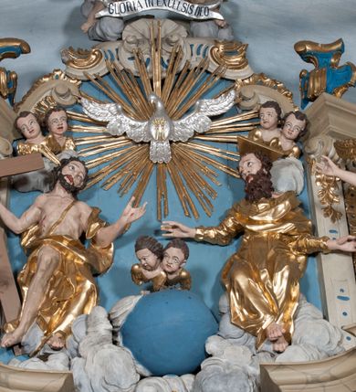 Zdjęcie nr 29: Nastawa ołtarzowa architektoniczna, jednoosiowa, jednokondygnacyjna ze zwieńczeniem, z bramkami i z rocaille'owymi uszami. Tabernakulum w formie zbliżonej do prostopadłościennej skrzynki, na wklęsło-wypukłym rzucie, ustawione na niskim cokole, o wypukłej ściance frontowej. Ujęte jest drewnianą obudową o wklęsłych bokach, flankowane parą ustawionych pod kątem pilastrów, których trzony przyjmują formę wolut. Zwieńczenie tabernakulum w formie niewielkiego szczytu, na którym ustawiona jest pasyjka. Całość ujęta po bokach rocaille'owymi wolutami. Drzwiczki w kształcie stojącego prostokąta, zamknięte łukiem nadwieszonym. W polu, na niebieskim tle malowane przedstawienie kielicha z hostią. Nastawa ustawiona na zdwojonym cokole, o  wklęsłym przebiegu, ujęta dwiema parami kolumn na tle zwielokrotnionych pilastrów. Podpory dźwigają pełne belkowanie, wyłamane pośrodku. Pomiędzy podporami figury: po lewej św. Józefa, a po prawej św. Jana Chrzciciela, nad bramkami: po lewej św. Wojciecha, a po prawej św. Stanisława. Nad tabernakulum rocaille'owy kartusz z łacińską inskrypcją w polu. W polu środkowym nisza w formie stojącego prostokąta, zamkniętego łukiem wklęsło-wypukłym z uskokami z obrazem „Święta Rozmowa”. Zwieńczenie w formie zbliżonej do stojącego prostokąta ujętego po bokach dwoma pilastrami, bogato ozdobione dekoracją rzeźbiarską. W polu przedstawienie Trójcy Świętej, flankowane przez parę aniołów siedzących na wolutowych przyczółkach. Całość zamyka para aniołków ze srebrną wstęgą z napisem „GLORIA IN EXCELSIS DEO”. Bramki z drzwiczkami w formie stojącego prostokąta, flankowane węgarami, zamknięte wolutowym łukiem z zatkniętymi na szczycie rzeźbami świętych. Drzwiczki dekorowane w polu dwiema płycinami. Całość nastawy silnie dekorowana ornamentyką rokokową. Kolumny ustawione na bazach, z kompozytowymi kapitelami, wewnętrzne srebrzone, do jednej trzeciej wysokości zdobione kanelowaniem zamkniętym pierścieniem, kolumny zewnętrzne marmoryzowane. Struktura polichromowana w kolorze beżowym, profilowania marmoryzowane, ornamentyka złocona.